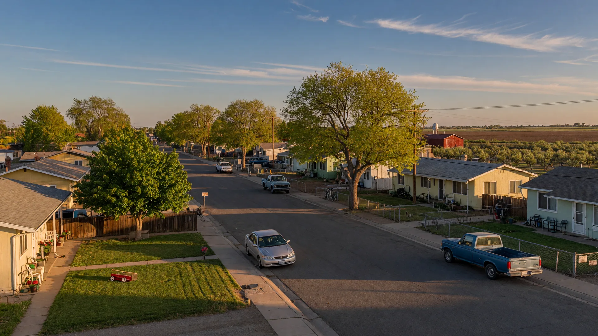 Quiet residential street in Winton, California with single-family homes, mature shade trees, and open farmland views in the background