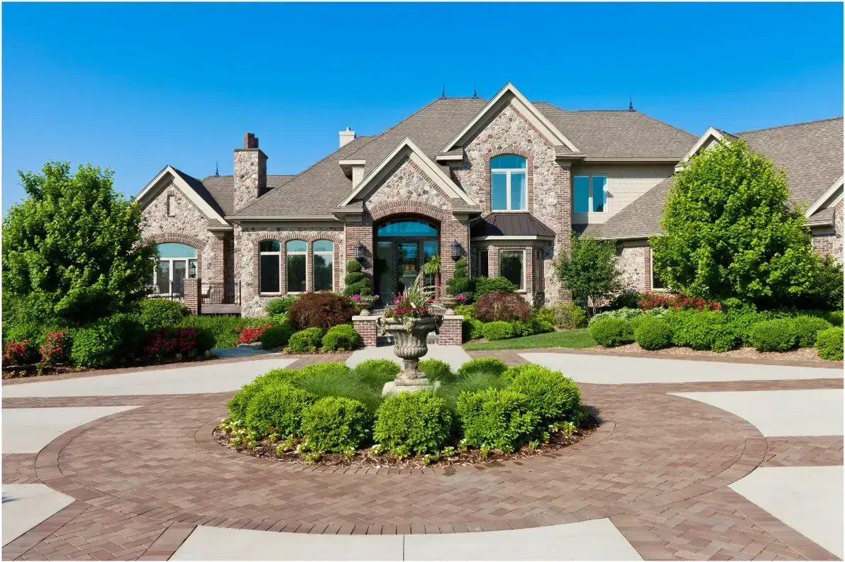 Luxury stone residence with circular driveway, fountain, and landscaped grounds.