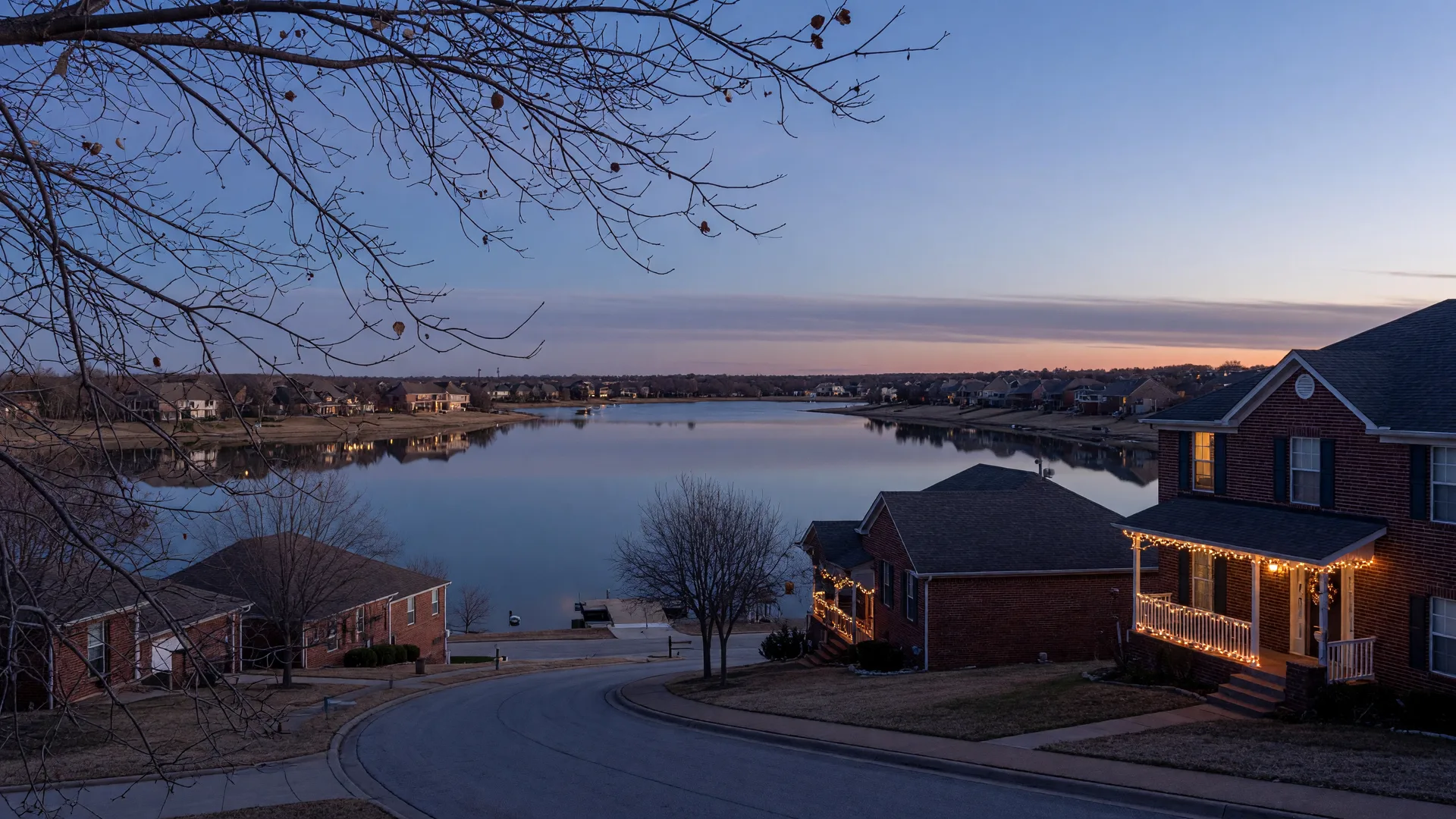 A North Texas lakeside suburb at dusk in early winter with a calm reservoir, bare trees, and warm porch lights