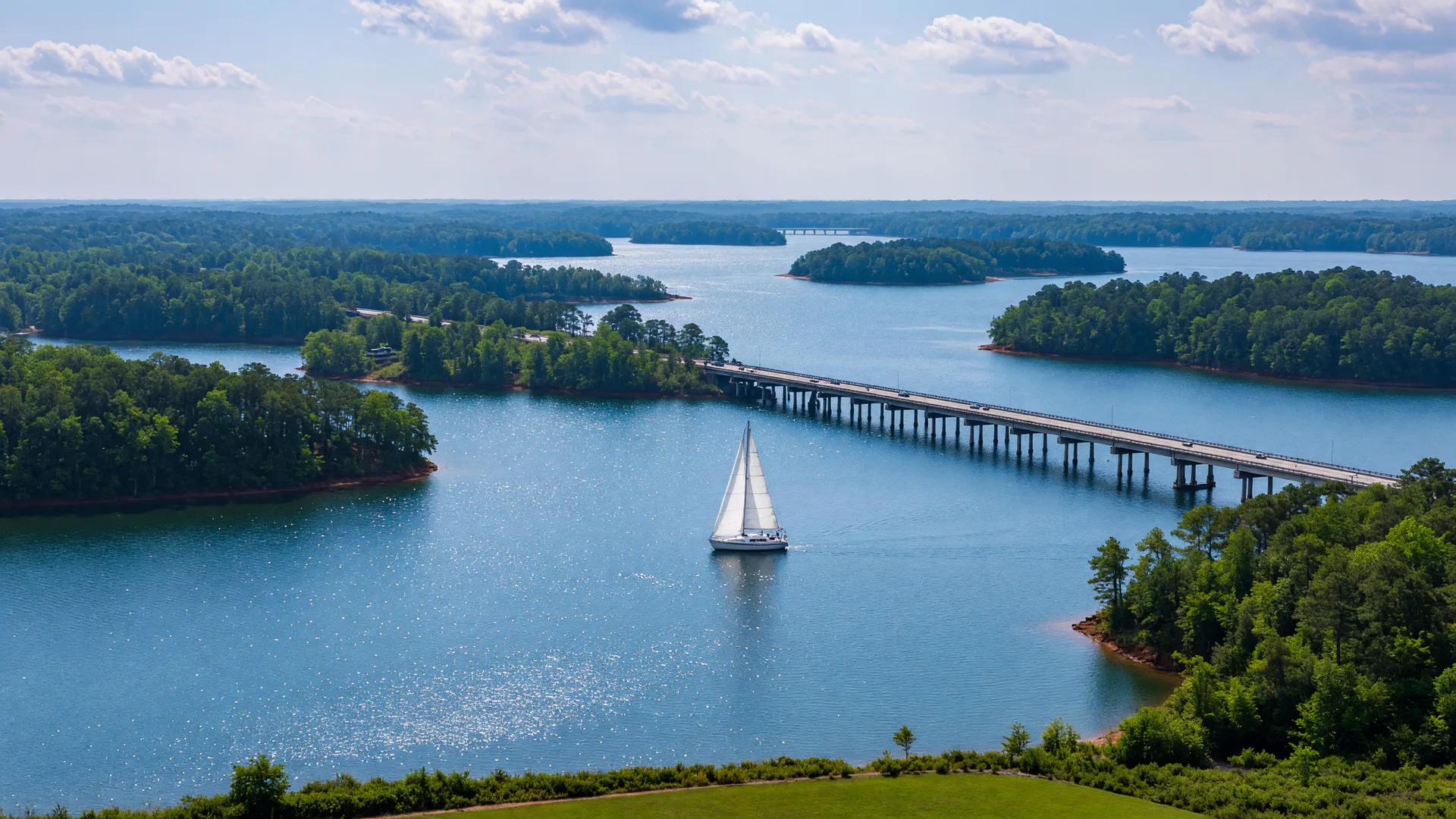 Bright morning view across the open water of Lake Norman with a sailboat under sail and tree-lined coves