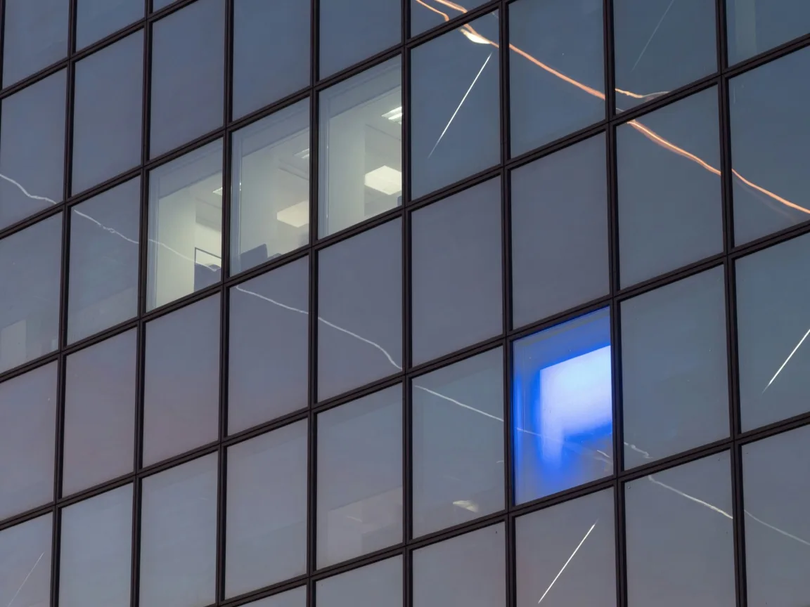 Glass skyscraper facade at dusk with one electric blue lit panel
