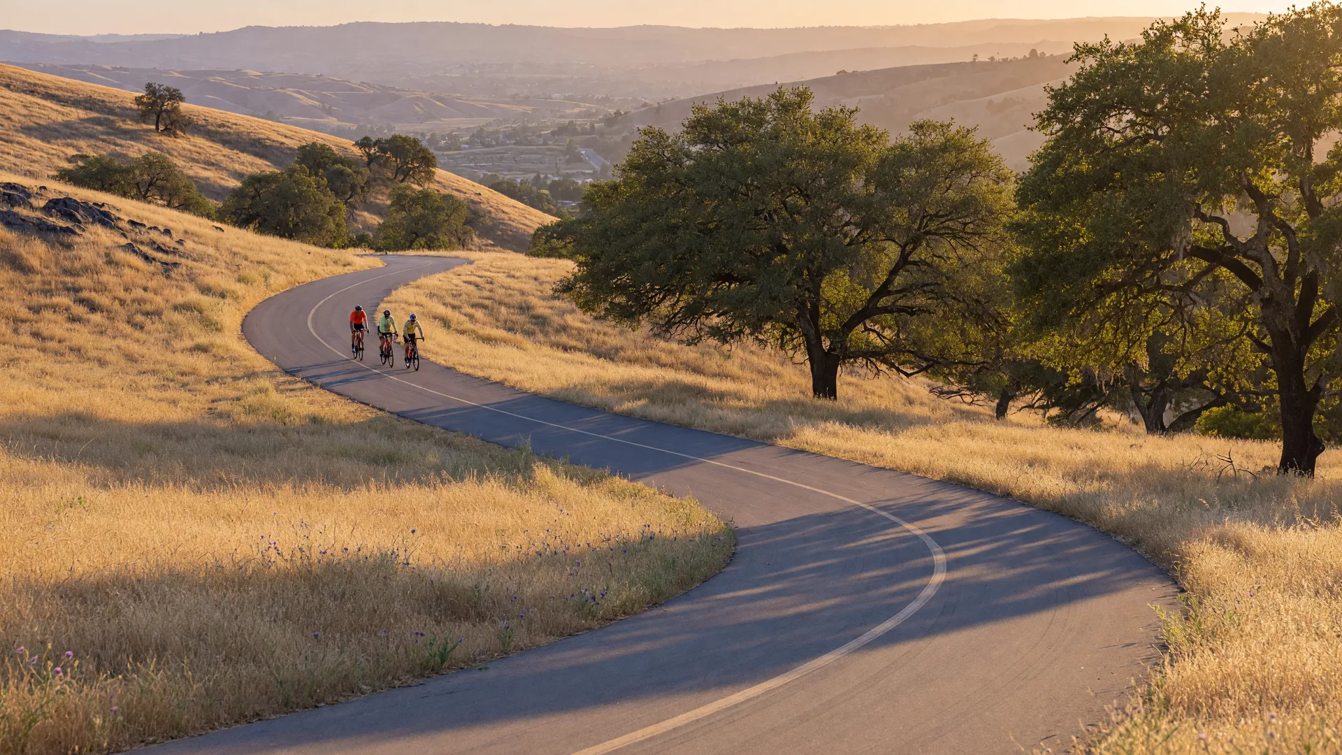 Cyclists riding along a curving paved path through golden foothills near Murrieta in warm late-afternoon light
