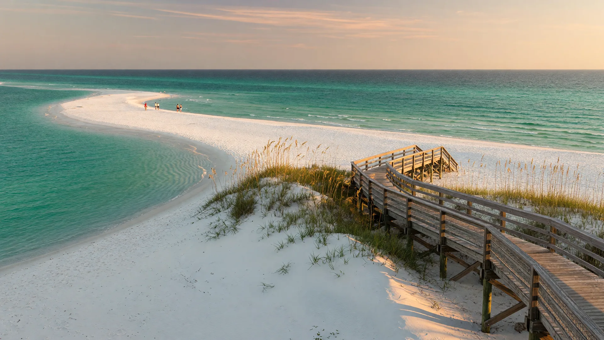 A Florida Panhandle beach at late afternoon with sugar-white sand, emerald Gulf water, and a wooden walkway over the dunes