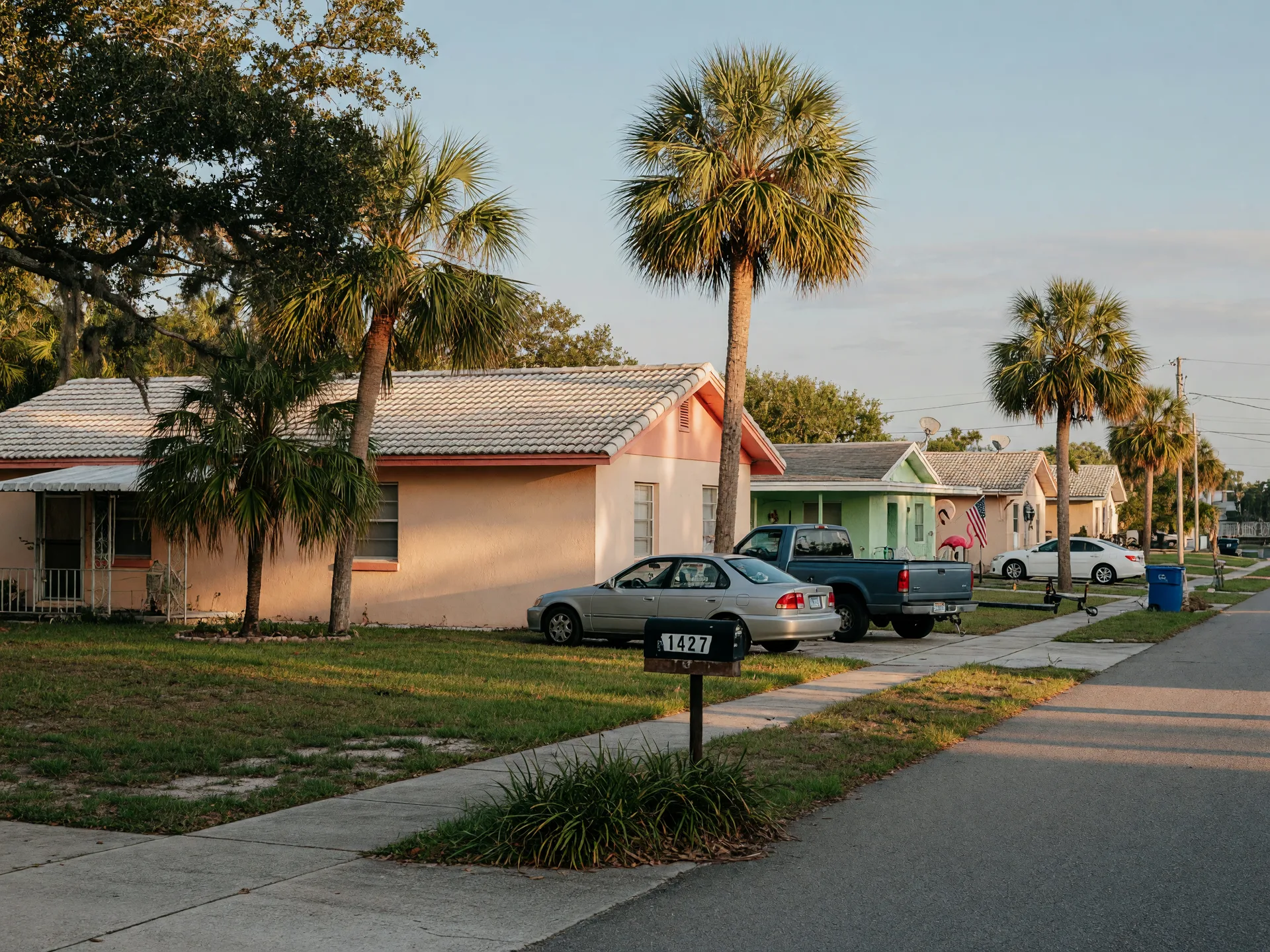Quiet street of single-story starter homes in Lee County, Florida with palms and a live oak in morning light