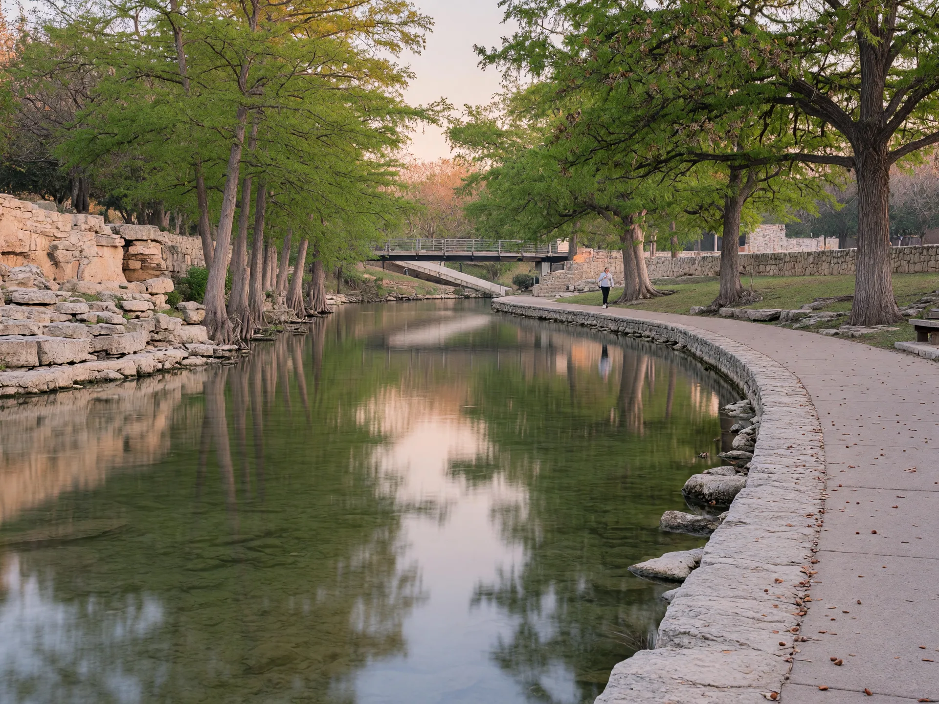 San Antonio River along the Mission Reach near the King William Historic District, showing clear water, cypress trees, and a pedestrian walking path in soft morning light