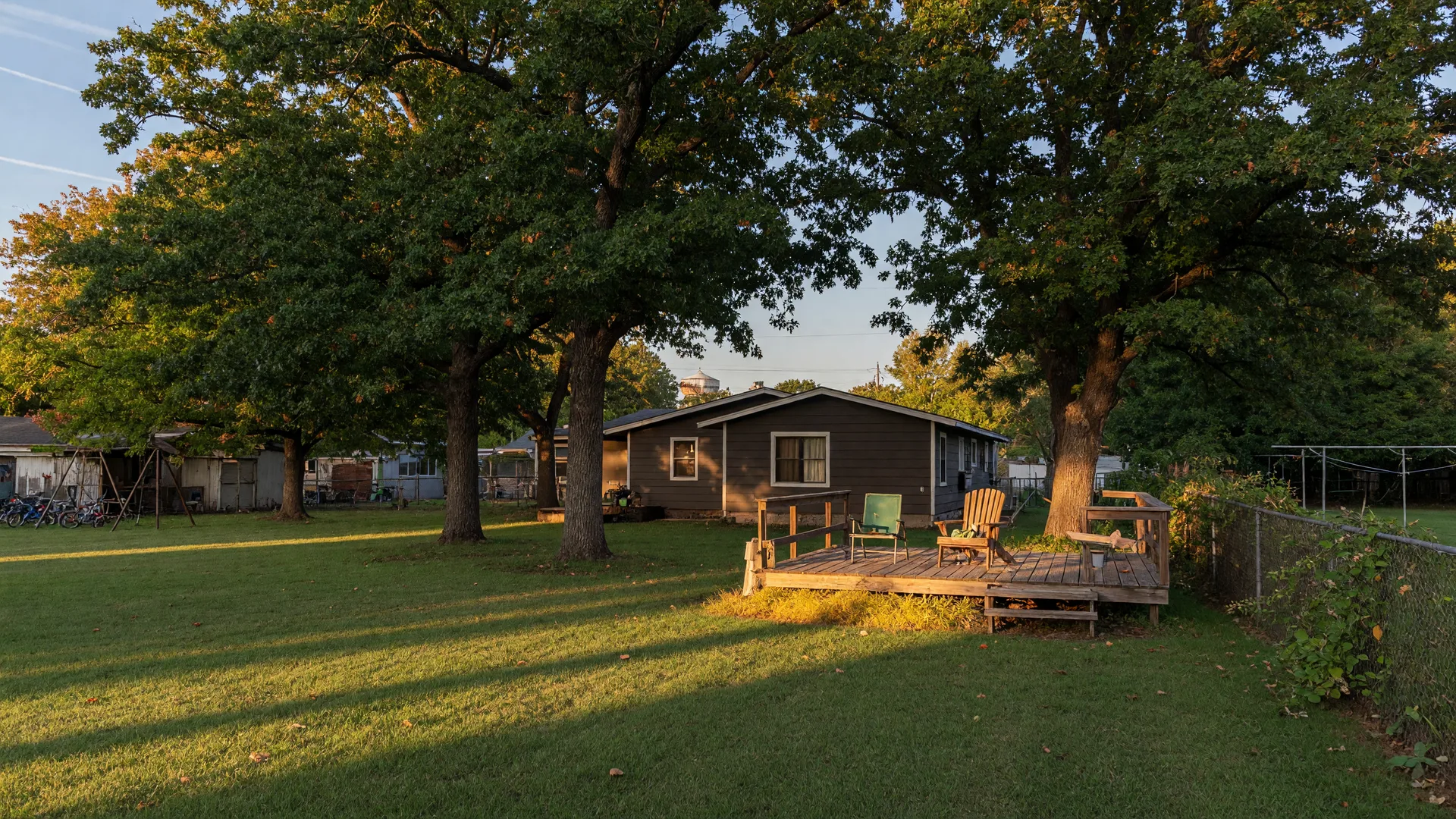 Tree-shaded one-acre yard with a wooden deck behind a dark-siding home in Omaha Texas in early autumn