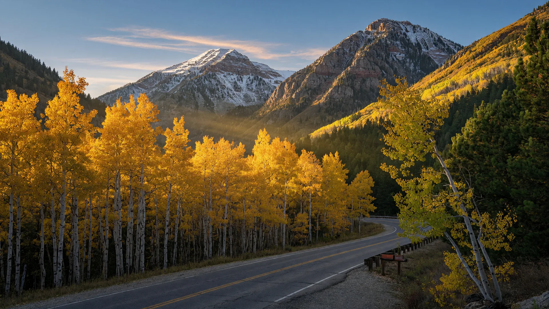 Golden aspens on a Utah mountainside at peak fall color, with green pines and snow-dusted peaks under a clear blue sky.