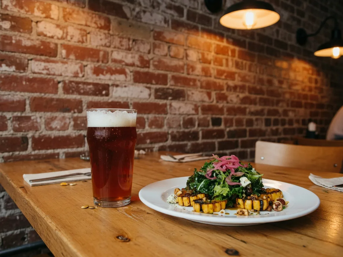 A cozy bistro table with a craft beer and a plate of seasonal food in warm interior light
