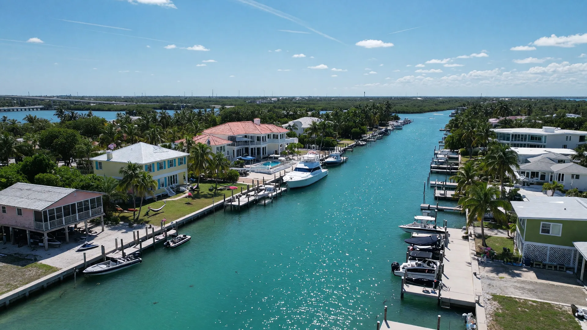 Aerial view of a Florida Keys canal neighborhood with a mix of waterfront stilt homes and larger estates with private docks along turquoise water