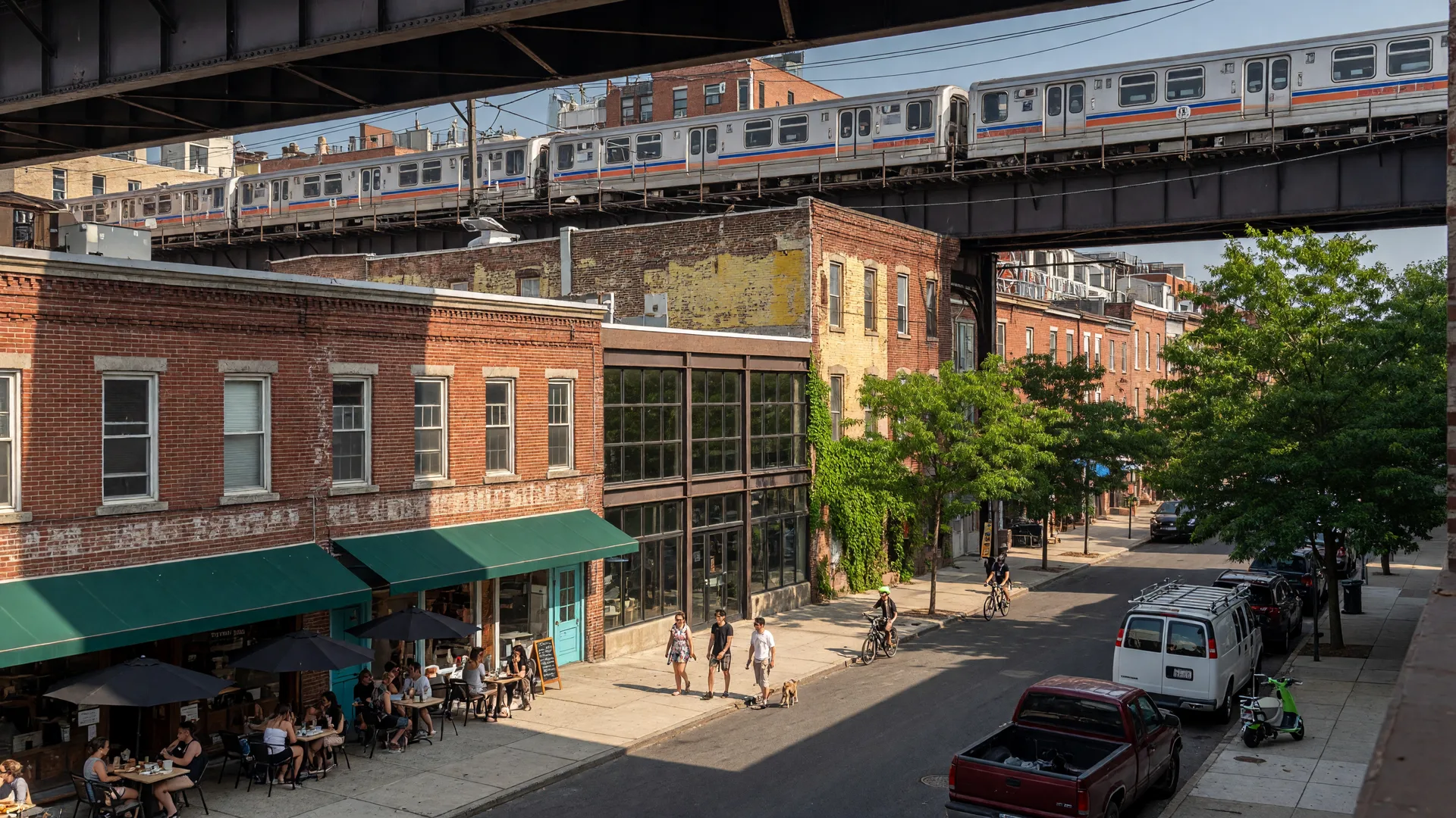 Frankford Avenue in Fishtown Philadelphia with the elevated SEPTA Market-Frankford Line train passing above a vibrant streetscape of brick warehouse buildings and sidewalk cafes