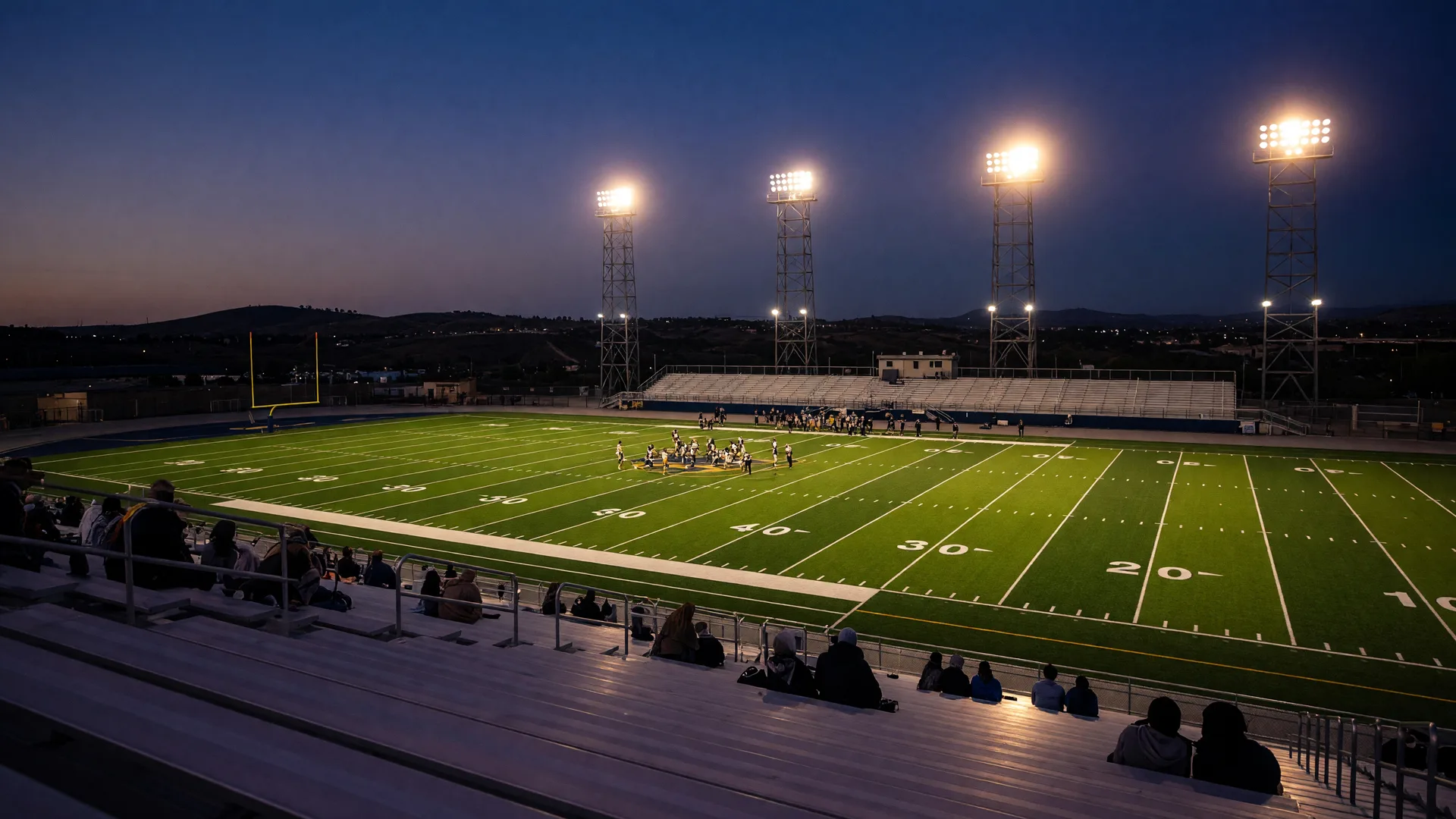 High school football stadium under Friday night lights with floodlights glowing over the turf field