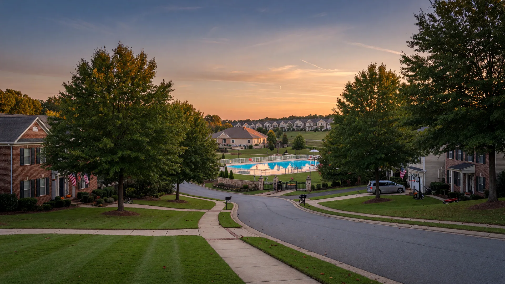 A quiet, tree-lined family suburb in east metro Atlanta with sidewalks and a gated community pool in the distance at golden hour