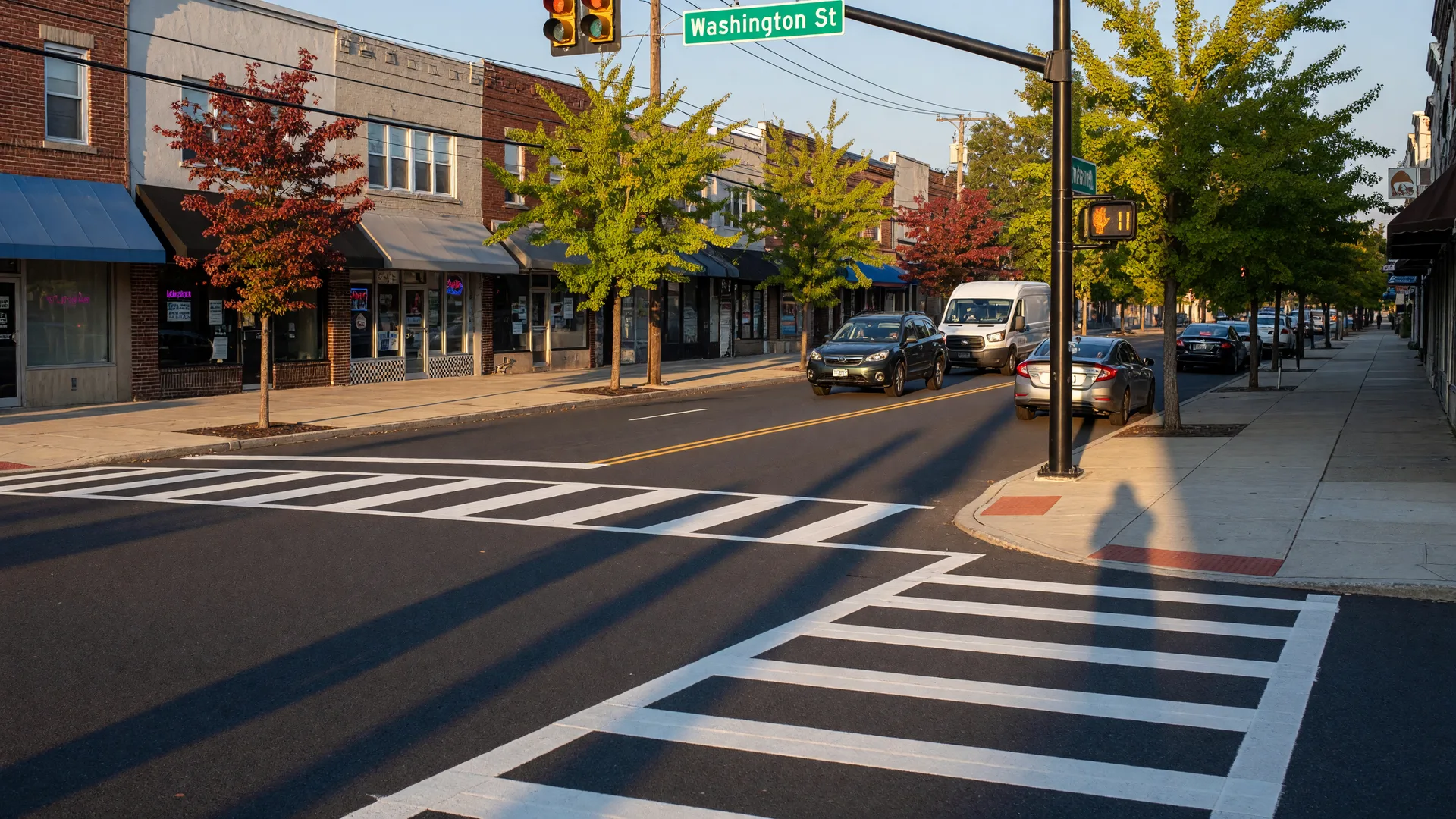 Washington Street in West Orange NJ on an October morning with freshly painted crosswalks, pedestrian signal poles with countdown timers, young street trees, and shop fronts along the corridor