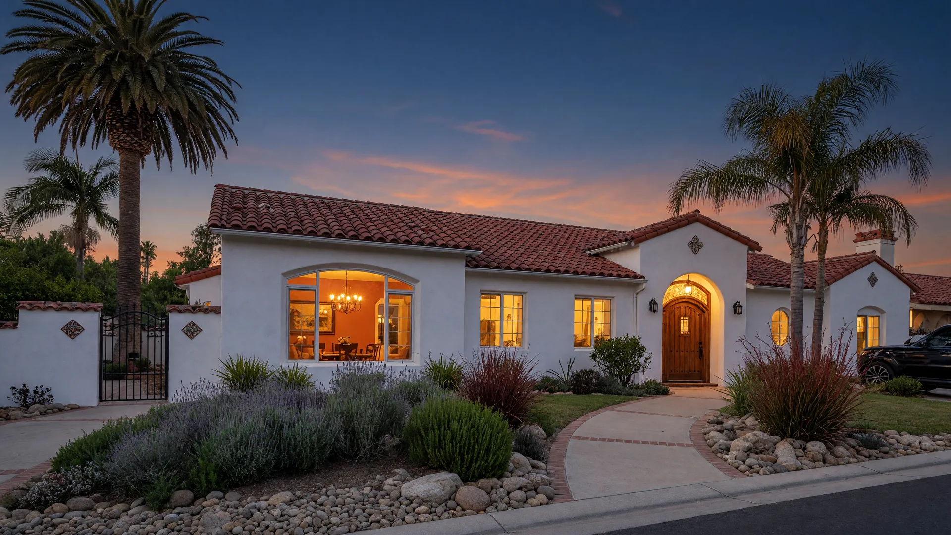 Southern California Spanish-style home exterior at dusk with warm lights glowing through the windows