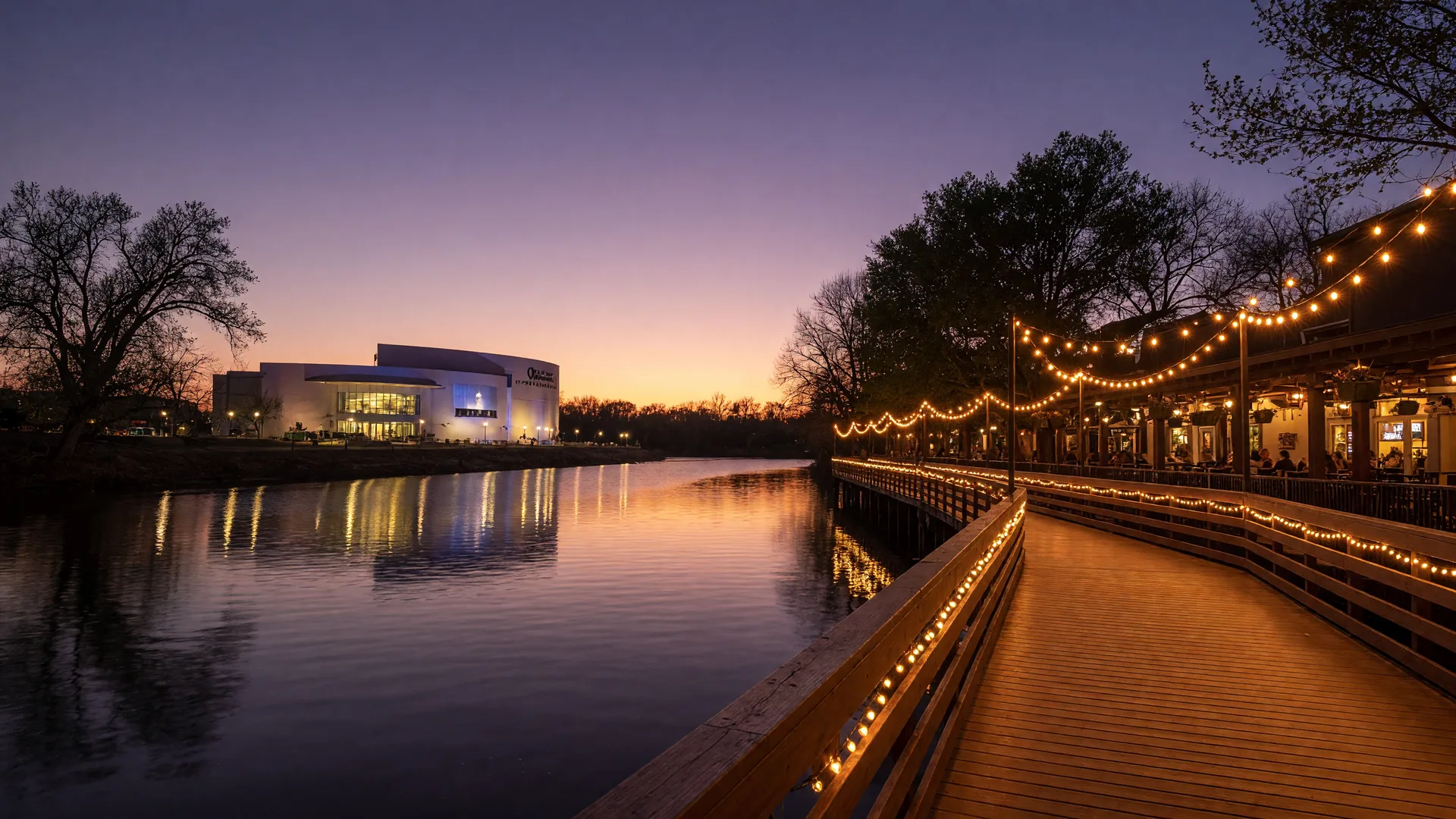 RiverWalk Crossing along the Arkansas River in Jenks, Oklahoma at dusk with warm lights reflecting on the water