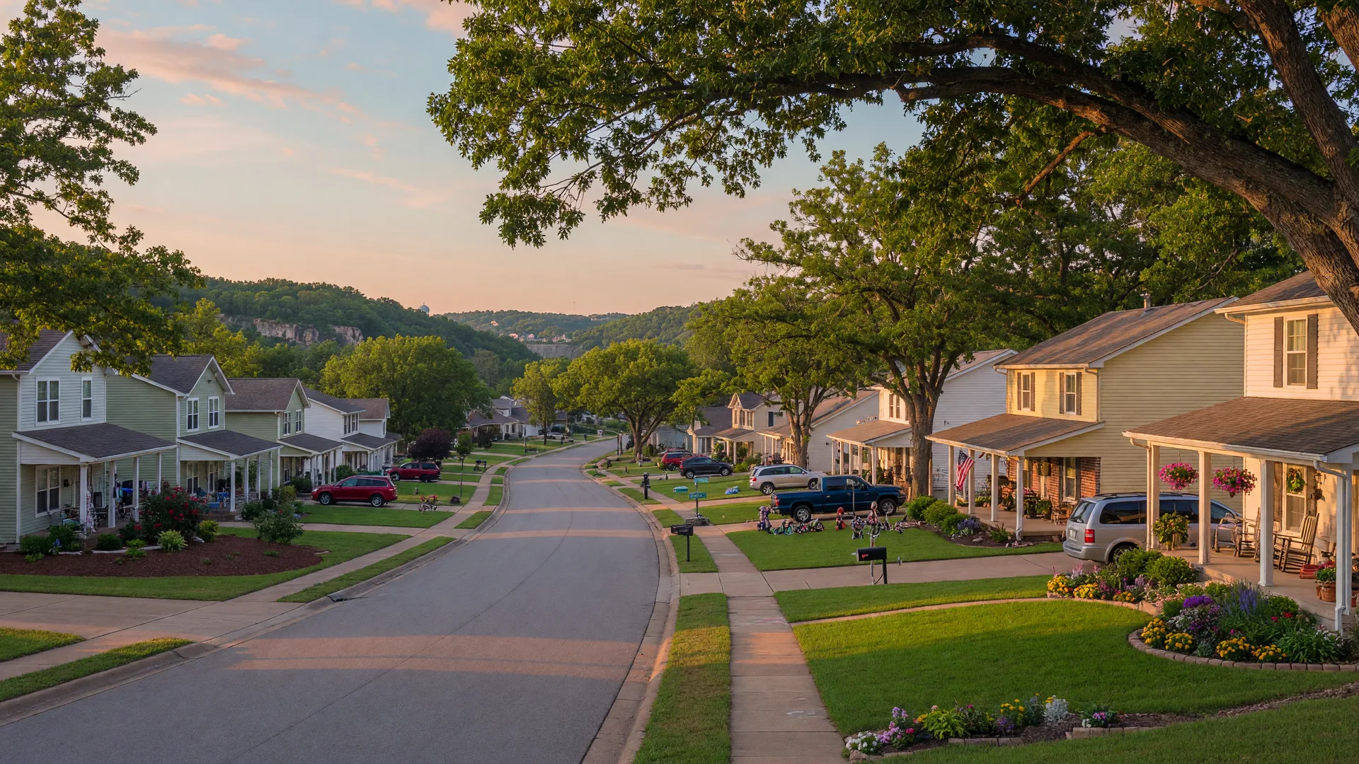 Tree-lined residential street in a Southwest Missouri community at golden hour, with family homes and rolling Ozark hills beyond