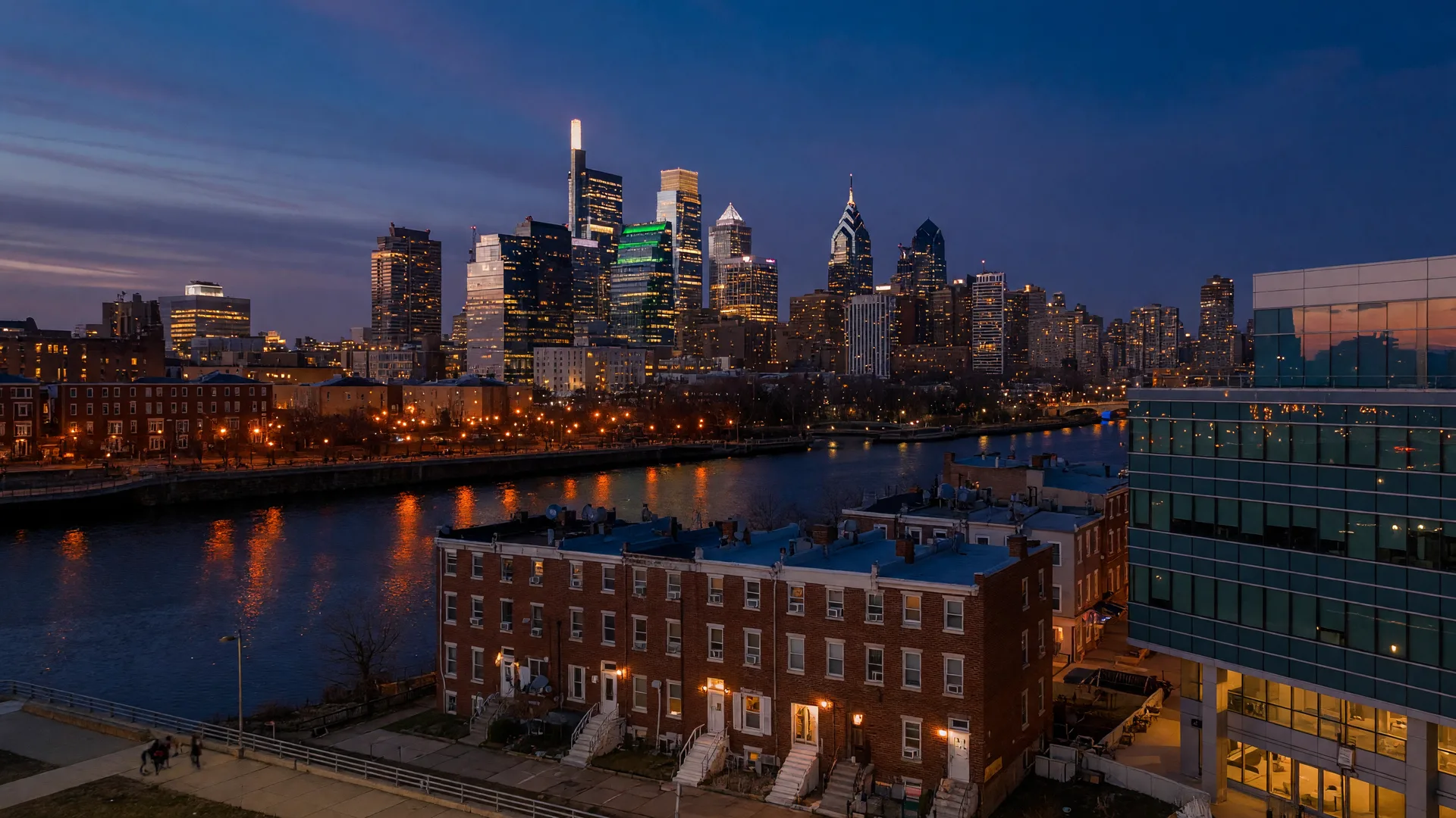Philadelphia skyline at dusk across the Schuylkill River with row homes in the foreground