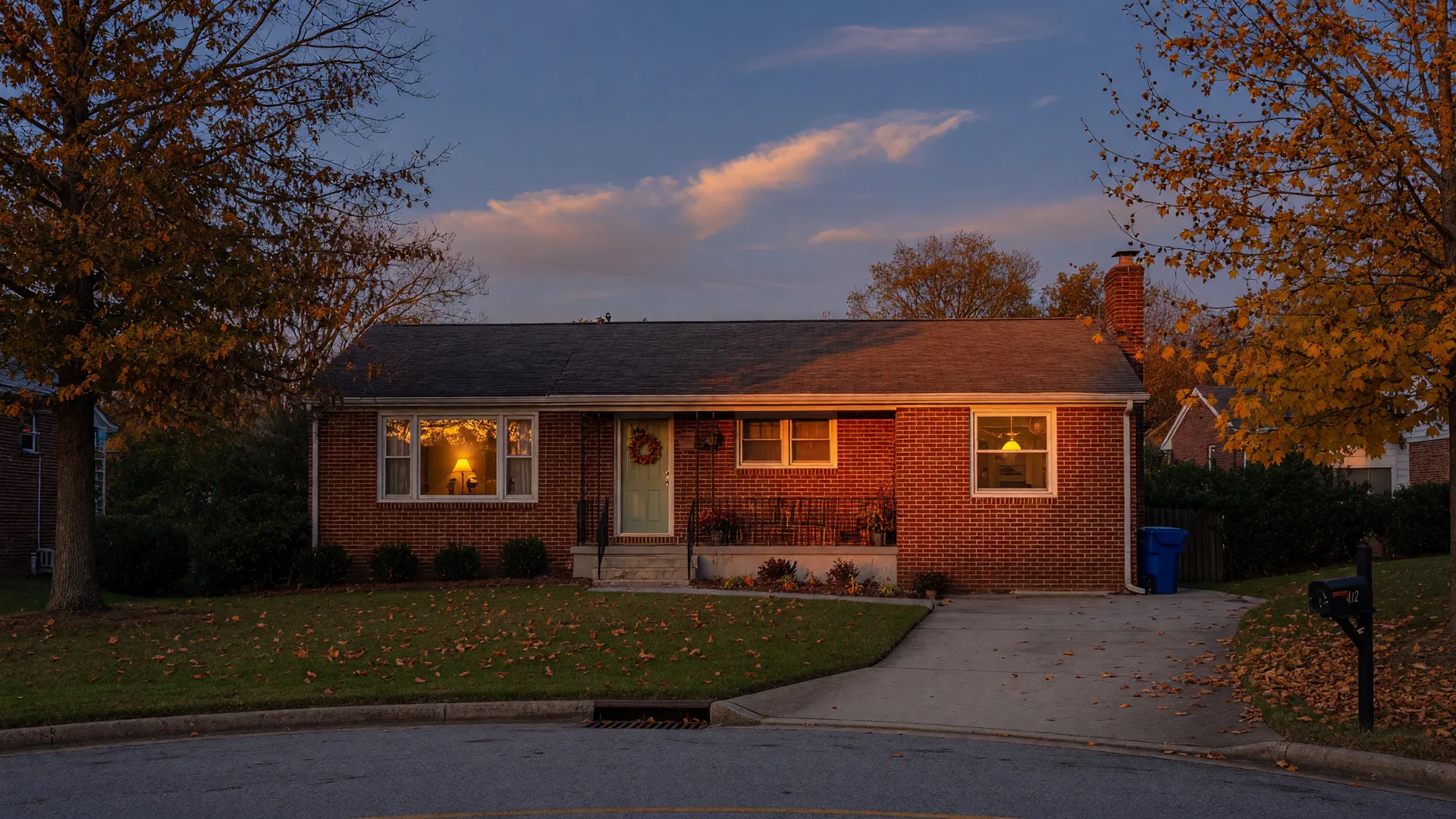 A classic brick-front suburban home in metro Atlanta at autumn dusk, warm interior lights glowing through the windows and amber leaves on the lawn, the kind of home a thoughtful buyer can actually afford at today's rates.