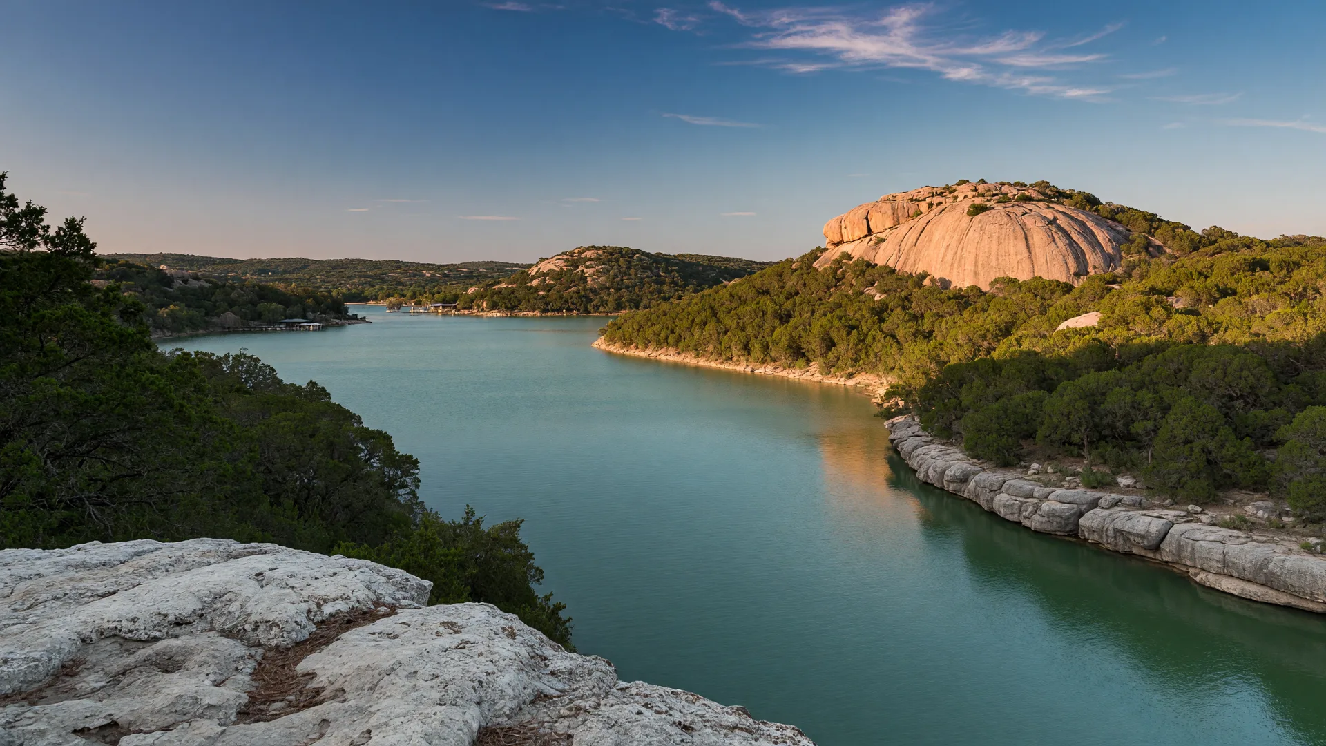 Golden-hour view of Lake Marble Falls on the Colorado River with calm green-blue water,rugged juniper-lined banks,and a distant granite outcrop