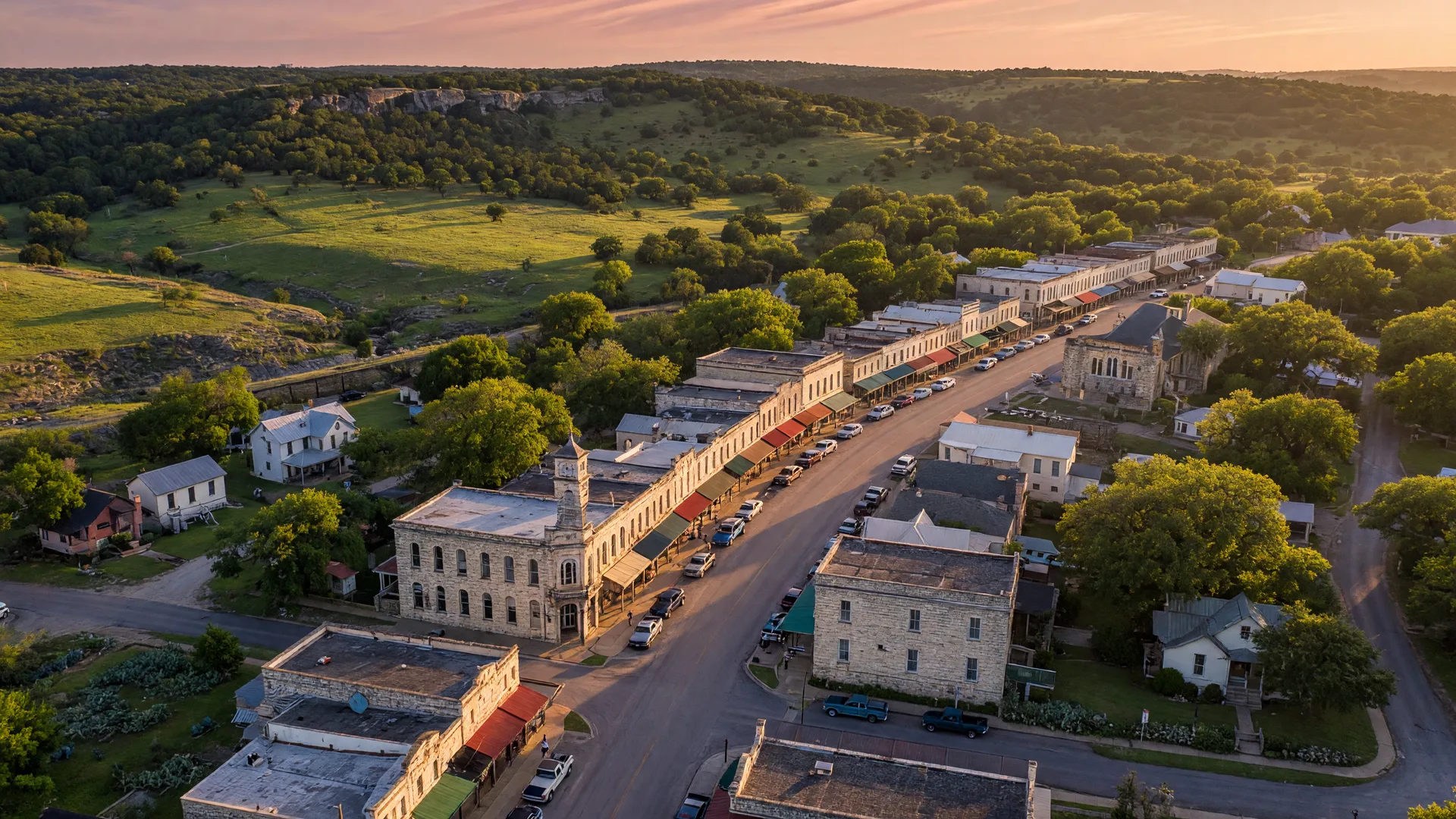 An aerial view of a charming Texas Hill Country town at golden hour with rolling hills