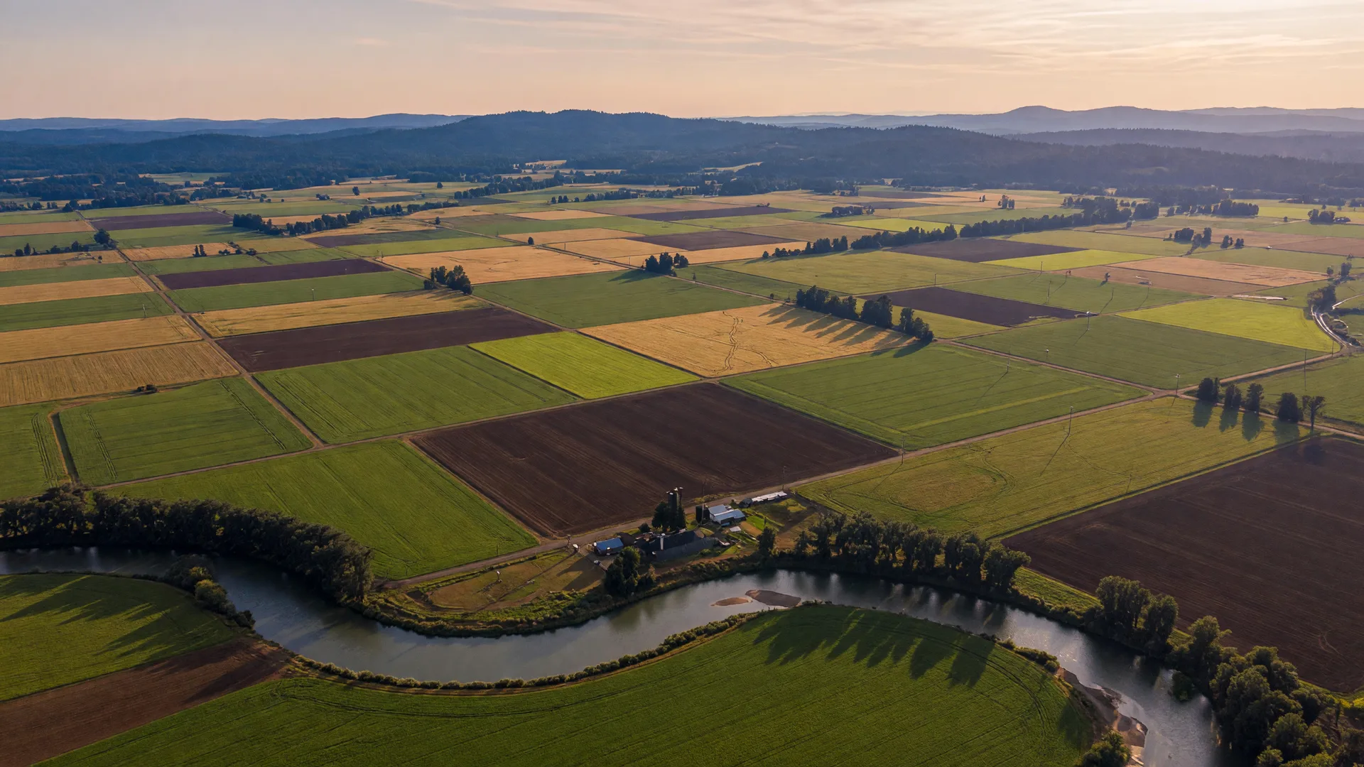 Aerial view of farm fields and a river winding through Oregon's Willamette Valley at golden hour