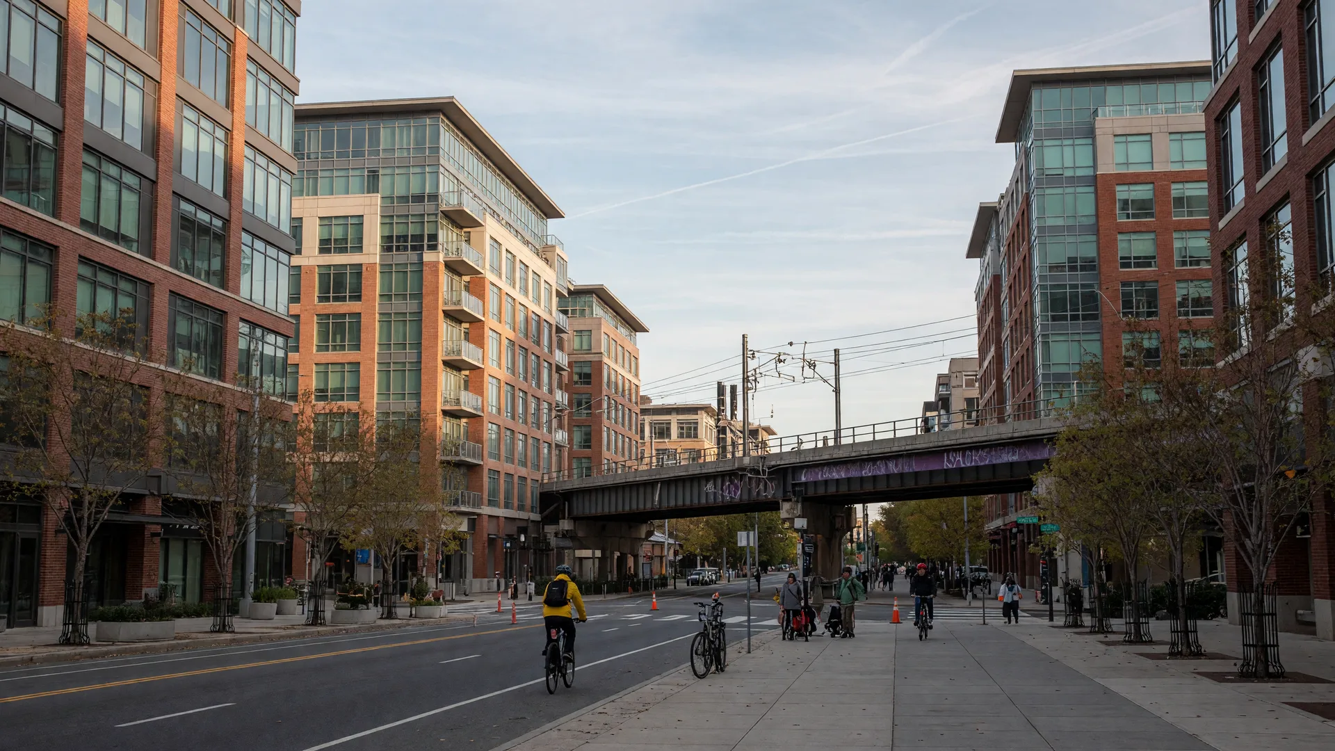 An Arlington transit corridor with glass and brick mid-rise buildings along a tree-planted avenue and an elevated rail bridge