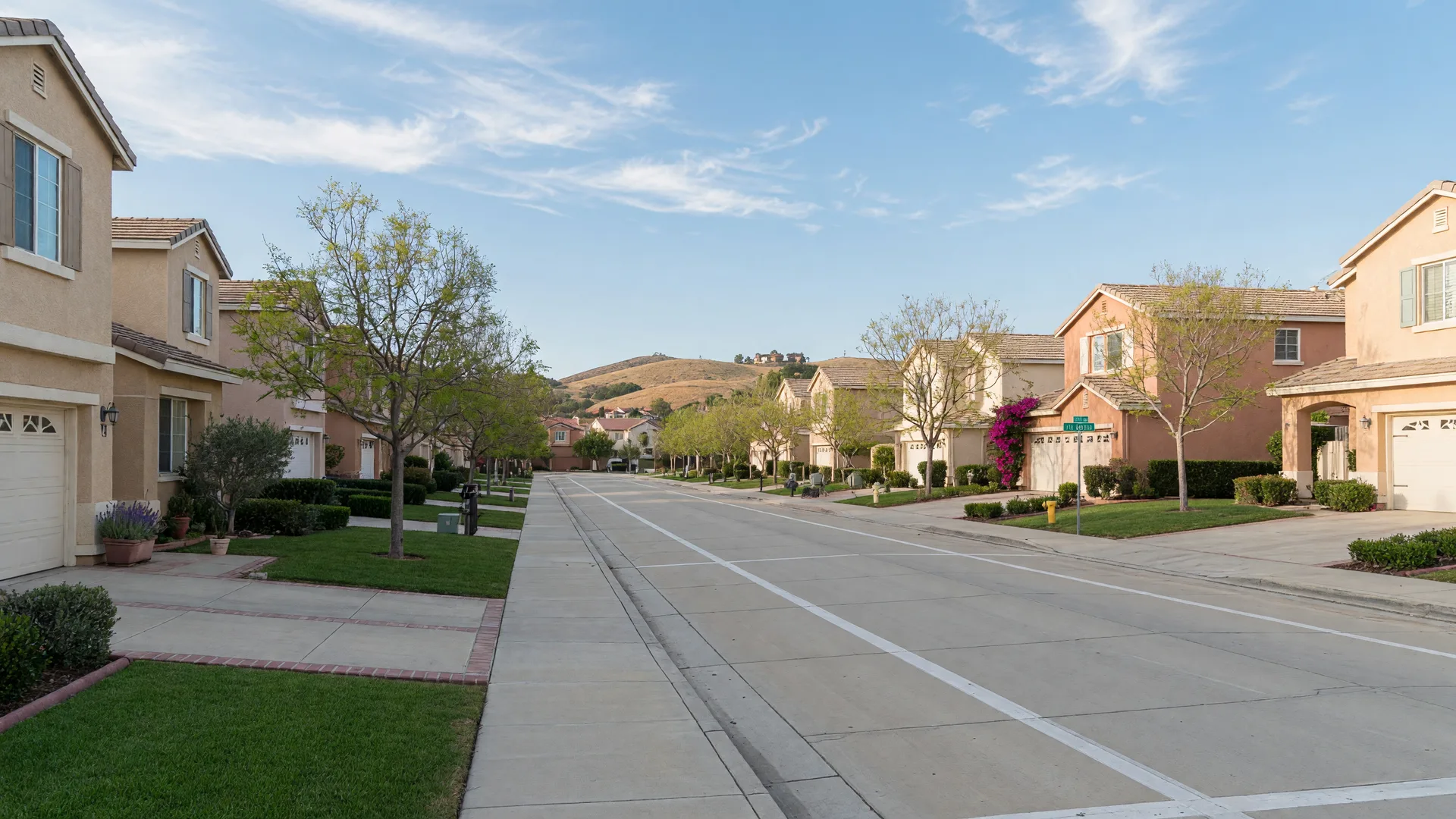 A quiet residential street with stucco single-family homes and young trees in the Quartz Ranch community in Menifee
