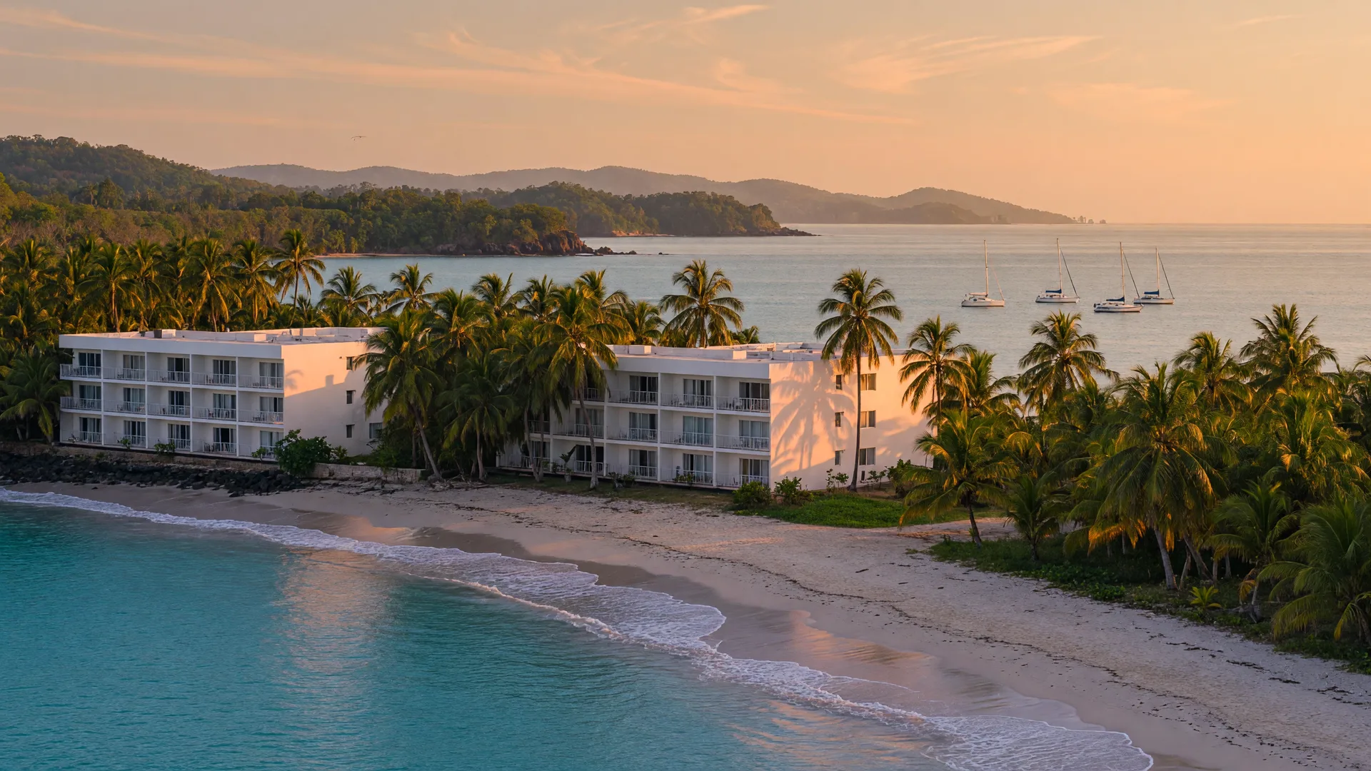 A golden-hour view of a modern beachfront condo among palm trees on a tropical Central American Pacific coastline, with calm turquoise water and distant green headlands