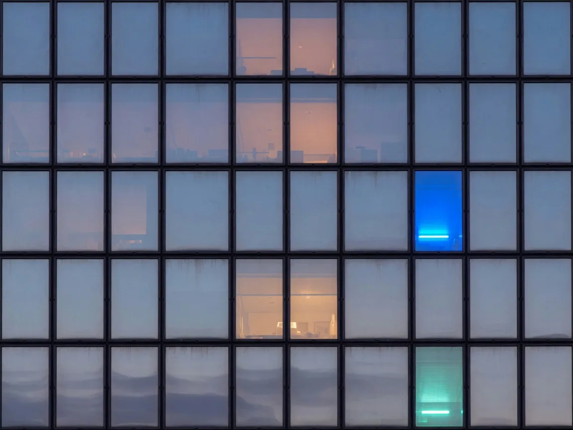 Close view of a glass tower facade at dusk, one pane glowing electric blue