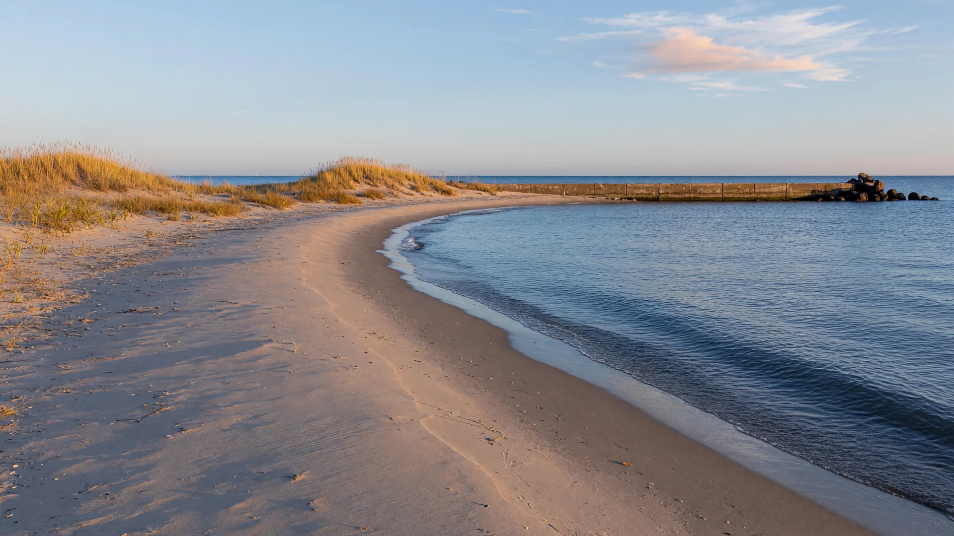 Lake Erie shoreline at Headlands Beach State Park in Mentor on a clear late-October afternoon, a wide natural sand beach with golden dune grass and a distant breakwall beside deep blue water
