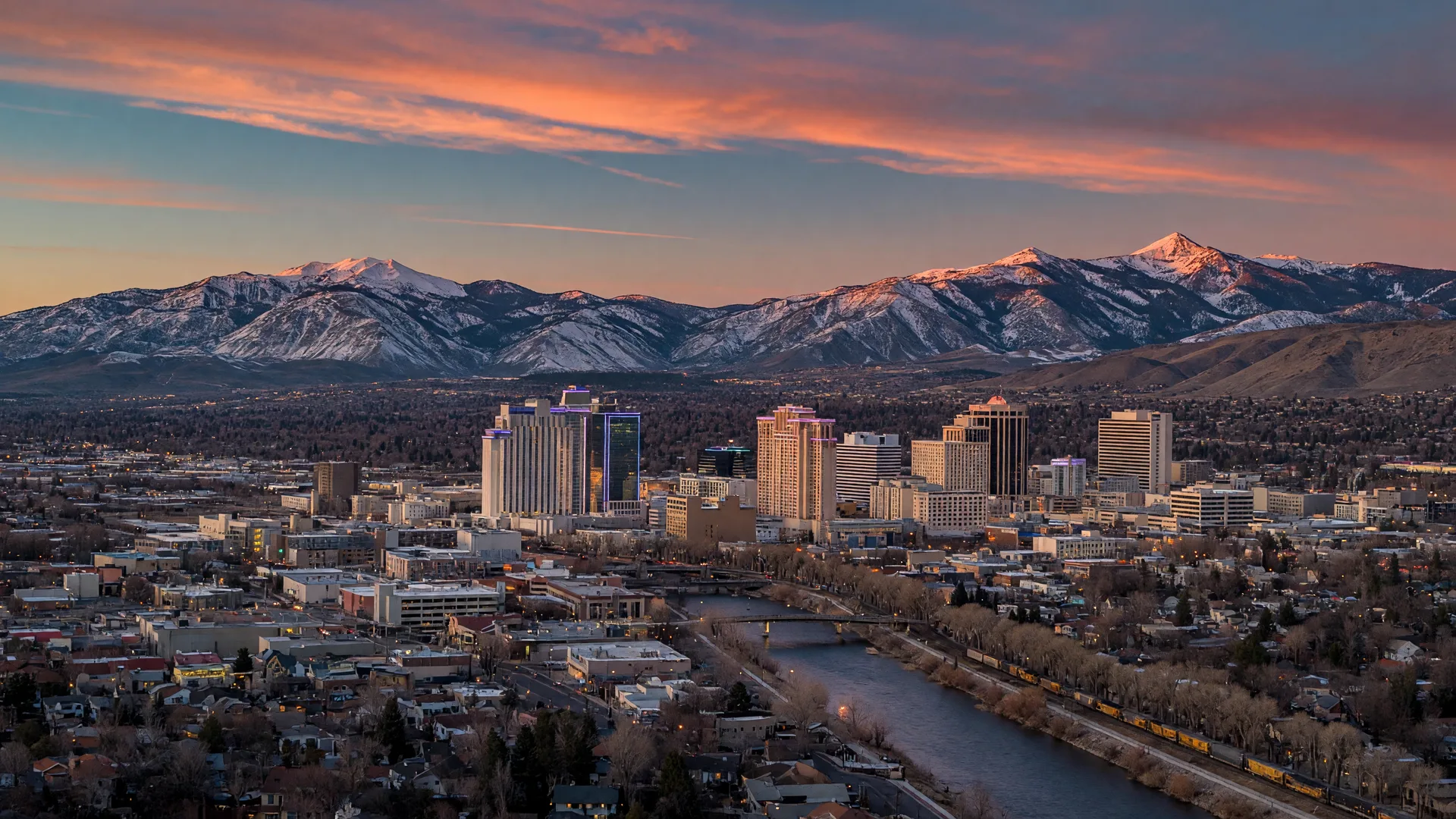 The Reno skyline at dusk,with the Sierra Nevada mountains behind the city and lights beginning to glow.