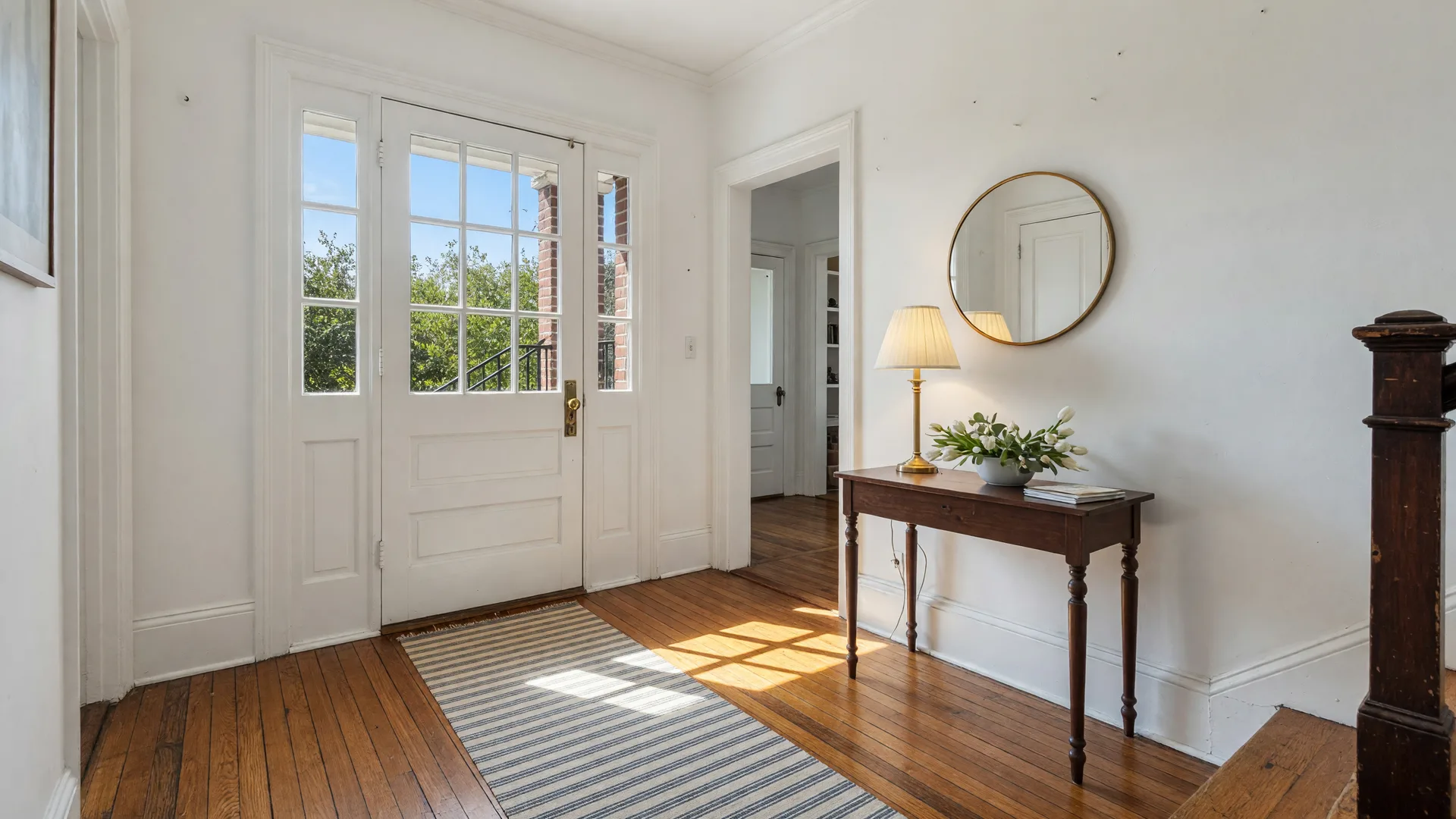 A bright, welcoming front entryway and foyer of a classic Philadelphia-area home with warm natural light and original hardwood floors, lightly staged for sale