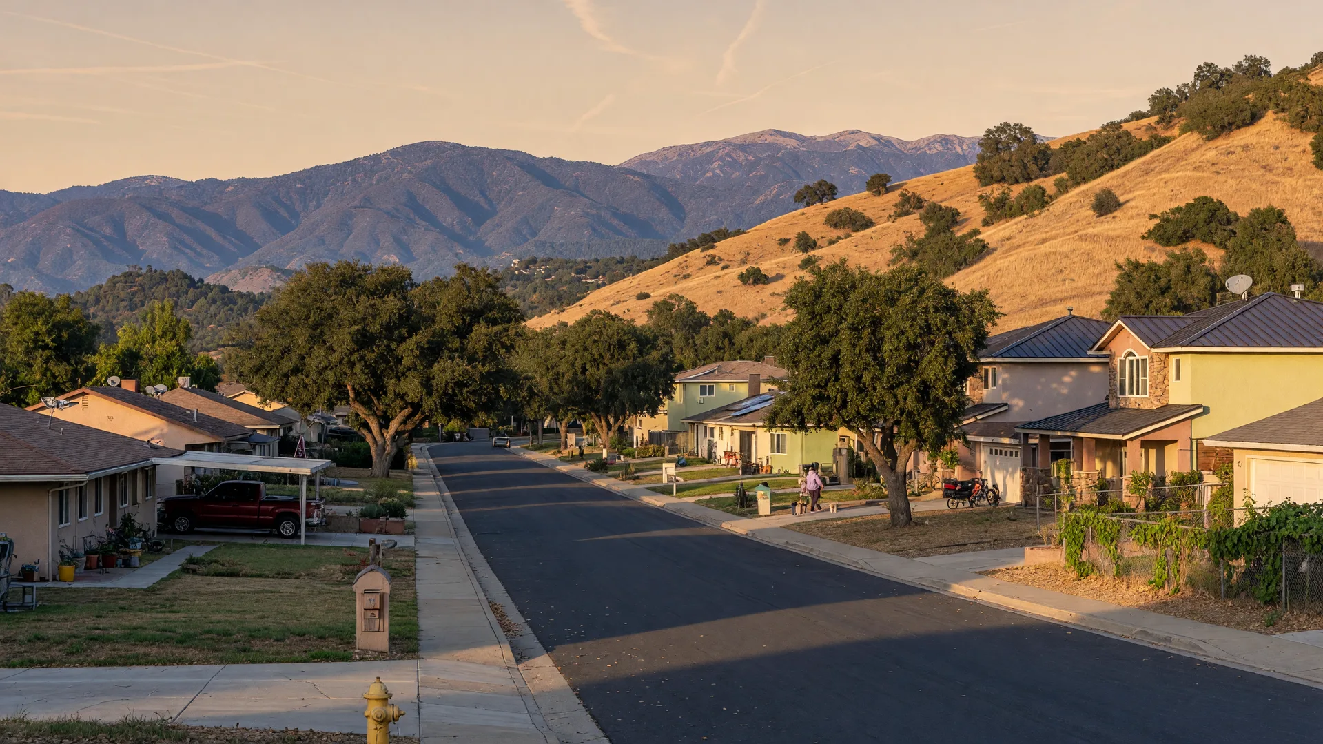 Golden-hour view of a quiet Yucaipa foothill street with ranch-style homes, oak trees, and the San Bernardino Mountains behind