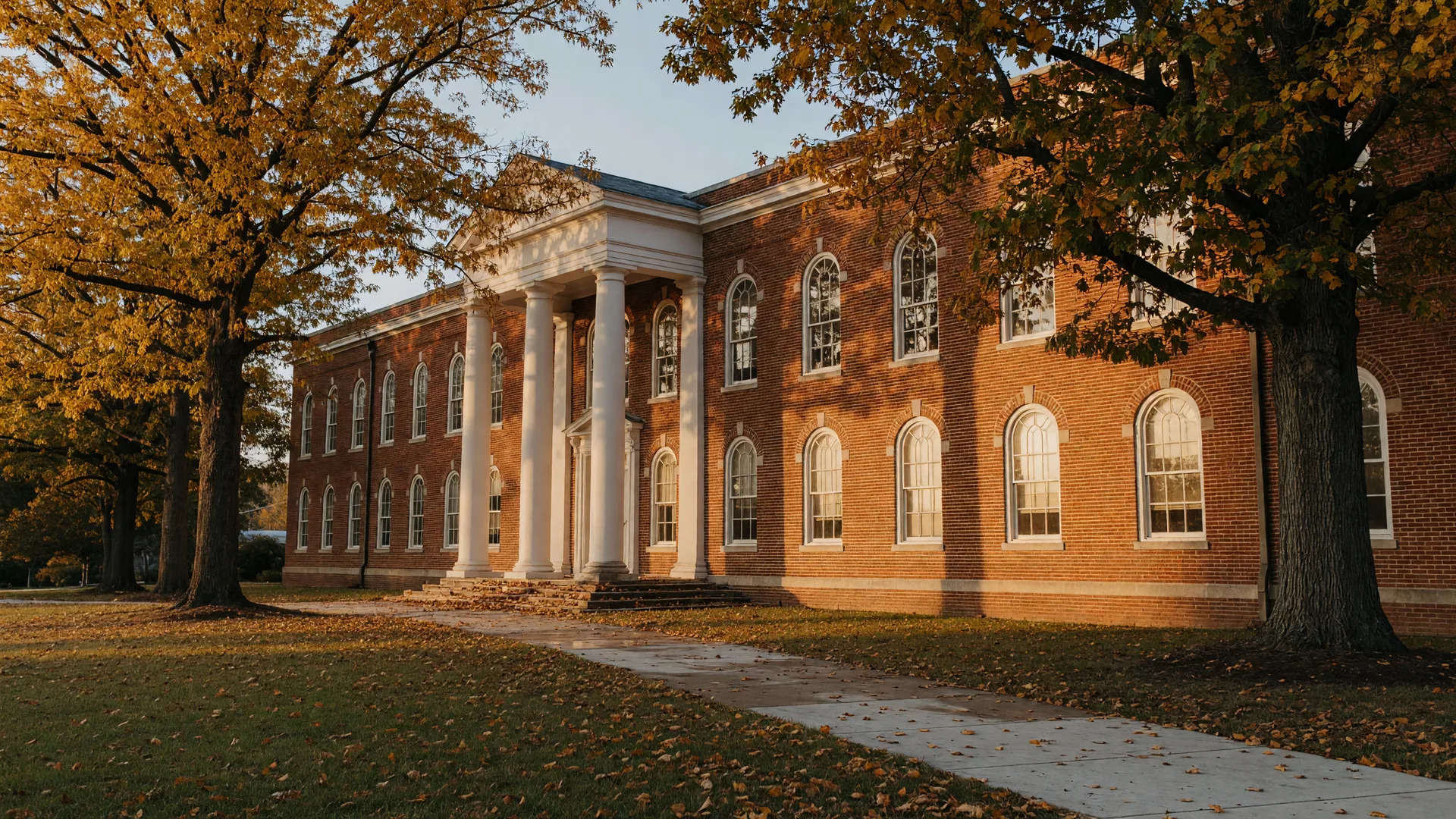 Golden autumn light on a stately red-brick school building with white columns and tall windows in a Knoxville-area neighborhood
