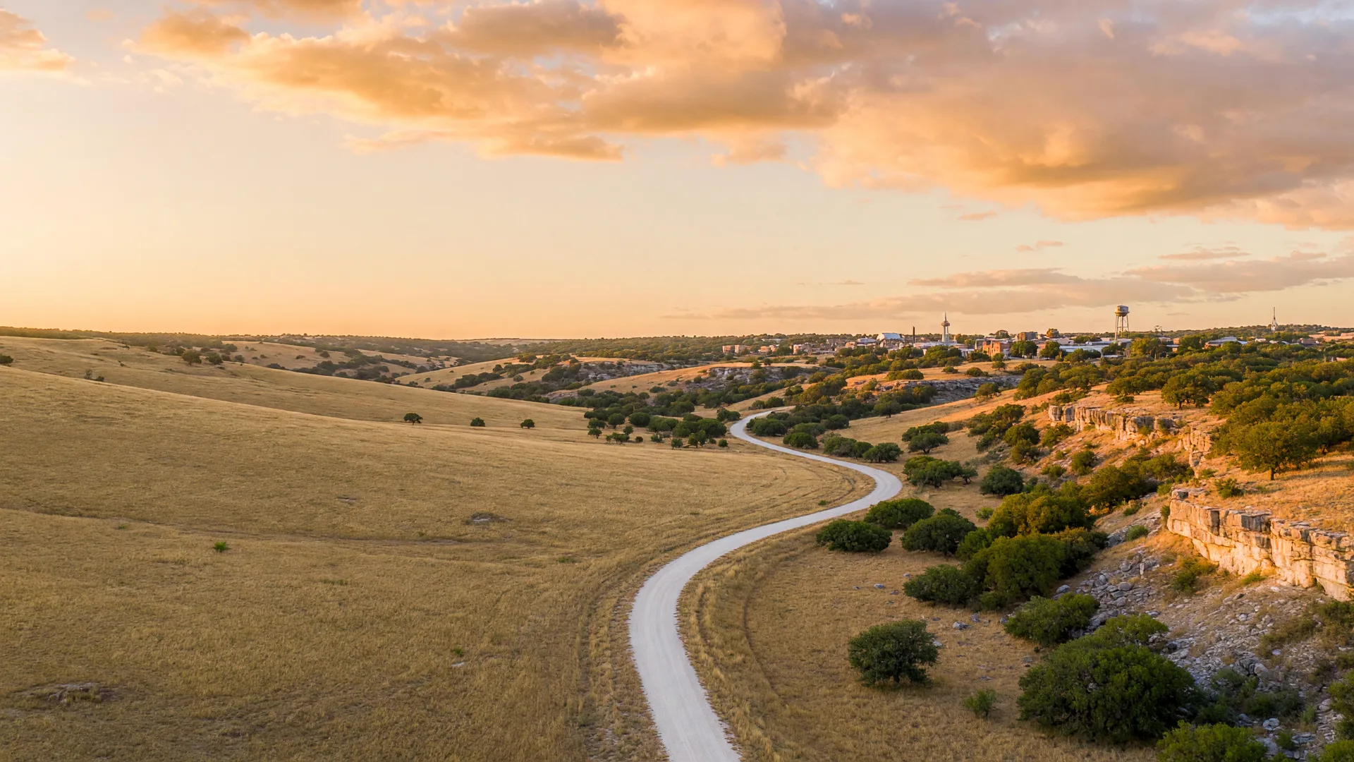 Aerial drone view of a ranch road winding through golden Texas Hill Country hills