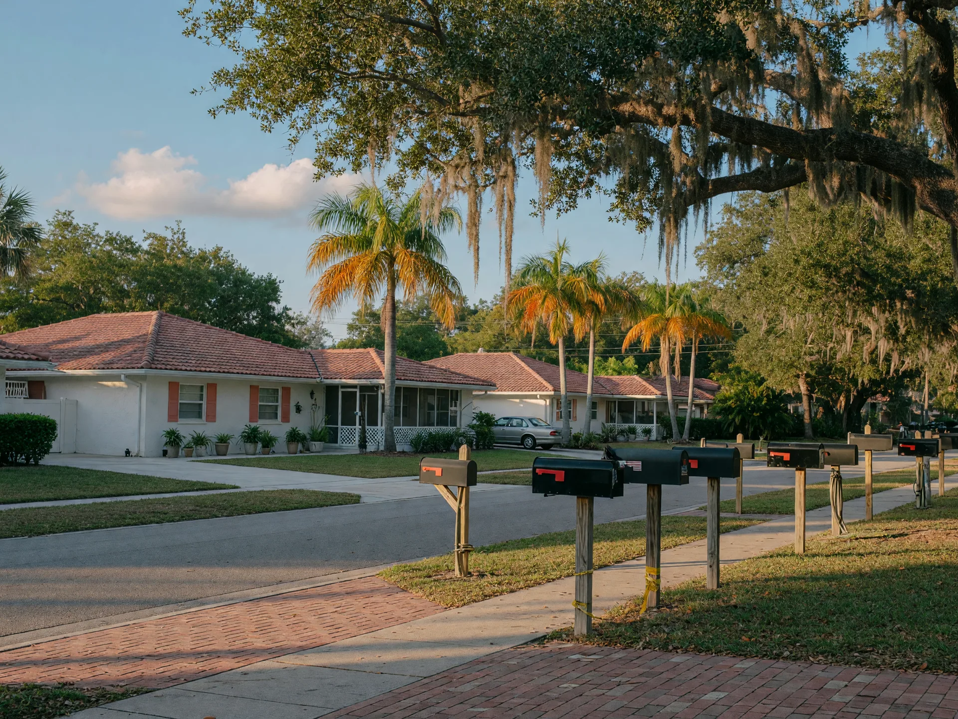 Tree-lined Naples neighborhood street with brick sidewalks and well-maintained Florida ranch homes under soft afternoon light