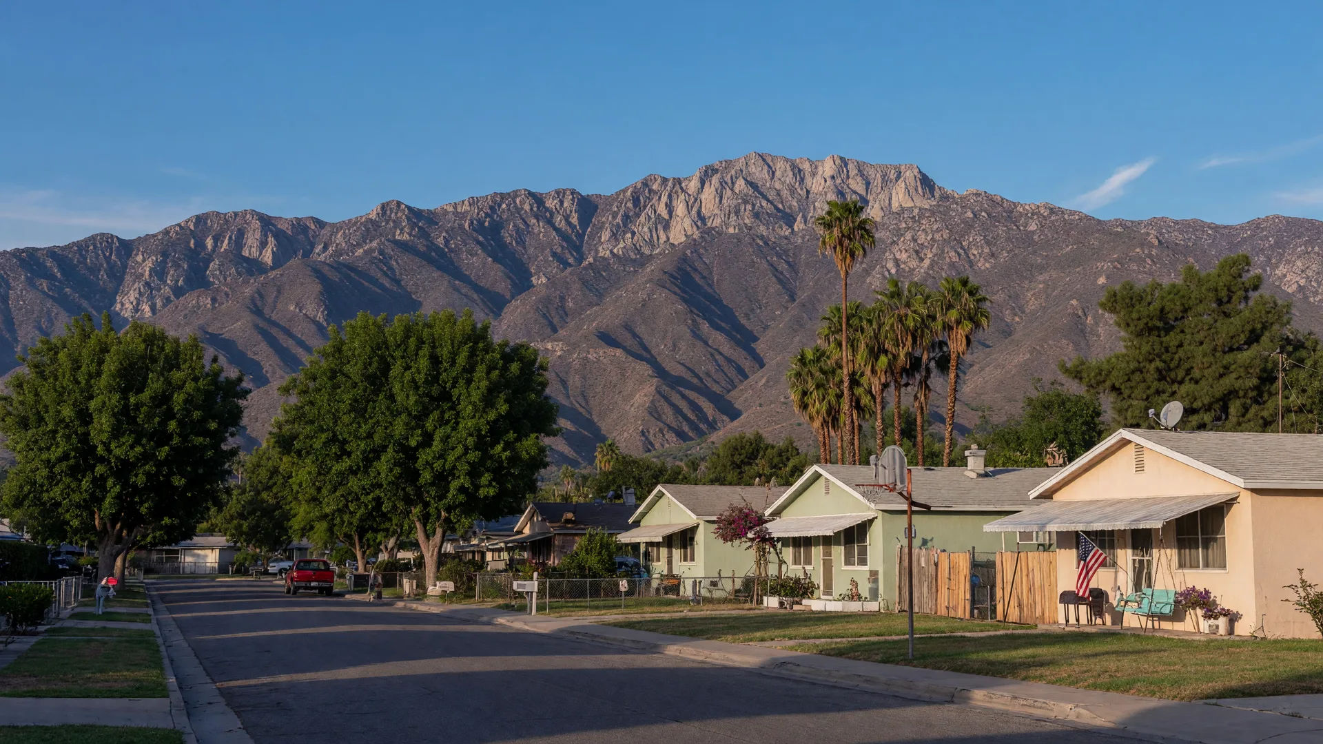 Quiet San Jacinto residential street with modest ranch homes and shade trees, the San Jacinto Mountains towering behind