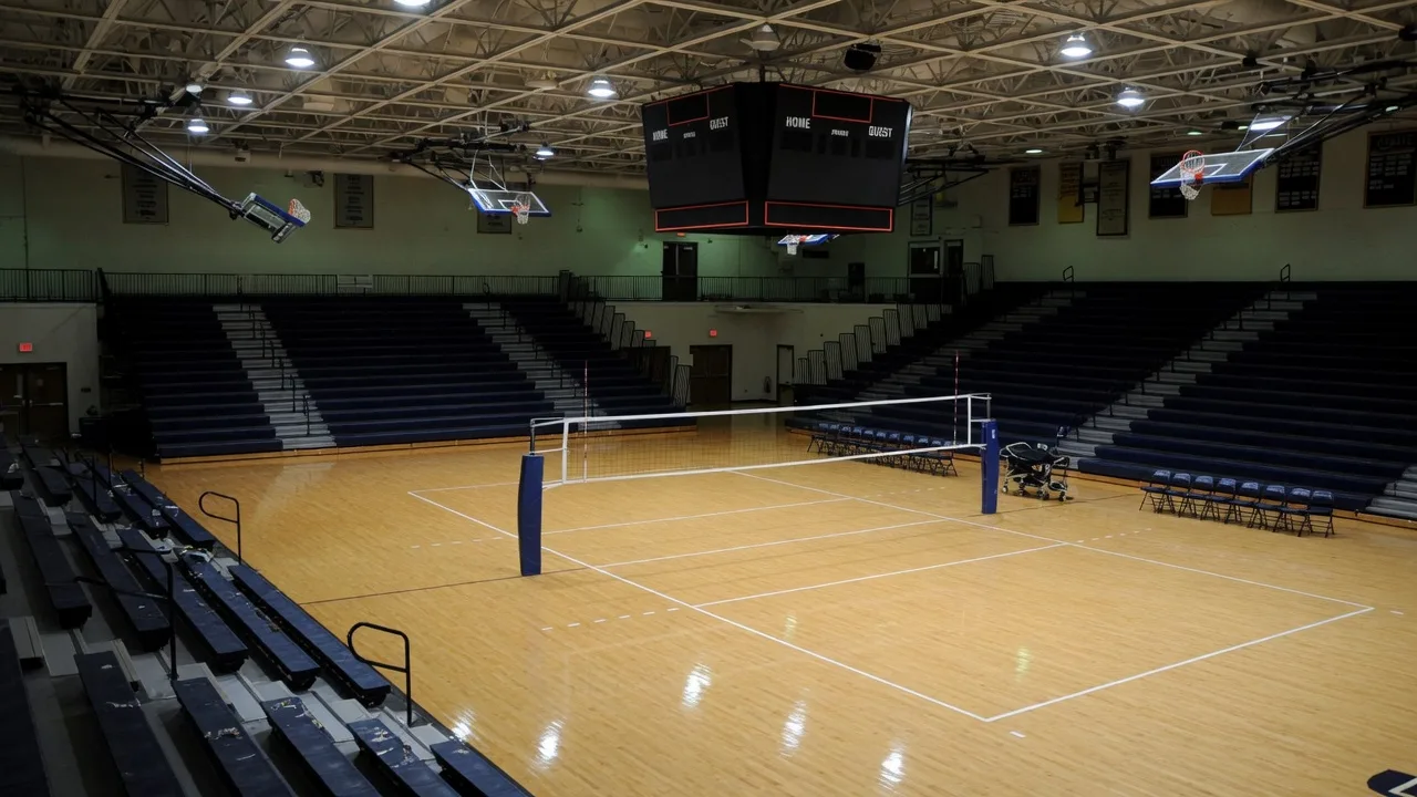 A college gymnasium with a volleyball net at center over a polished wood court