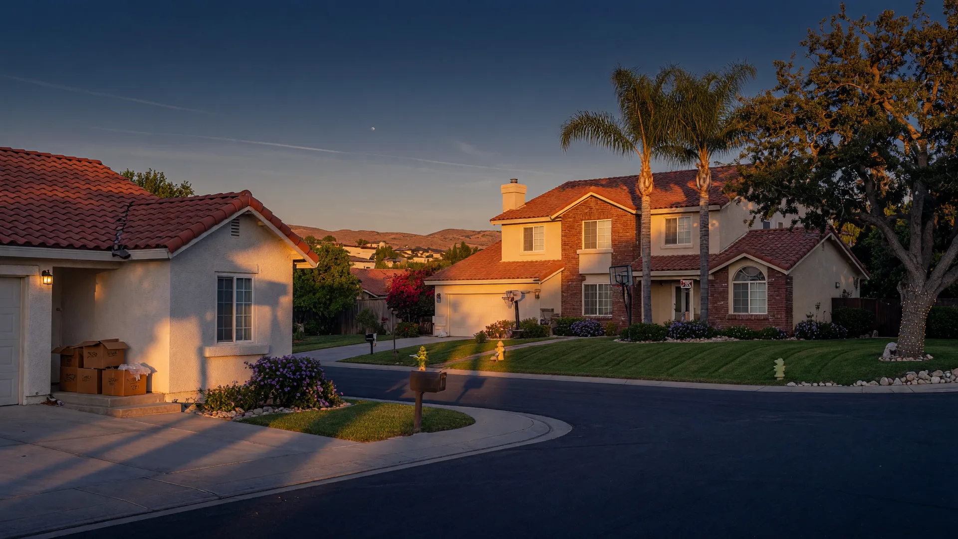 A sunny Murrieta cul-de-sac at golden hour with a modest single-story starter home and moving boxes in the foreground and a larger two-story family home with palm trees beyond, representing a growing family moving up