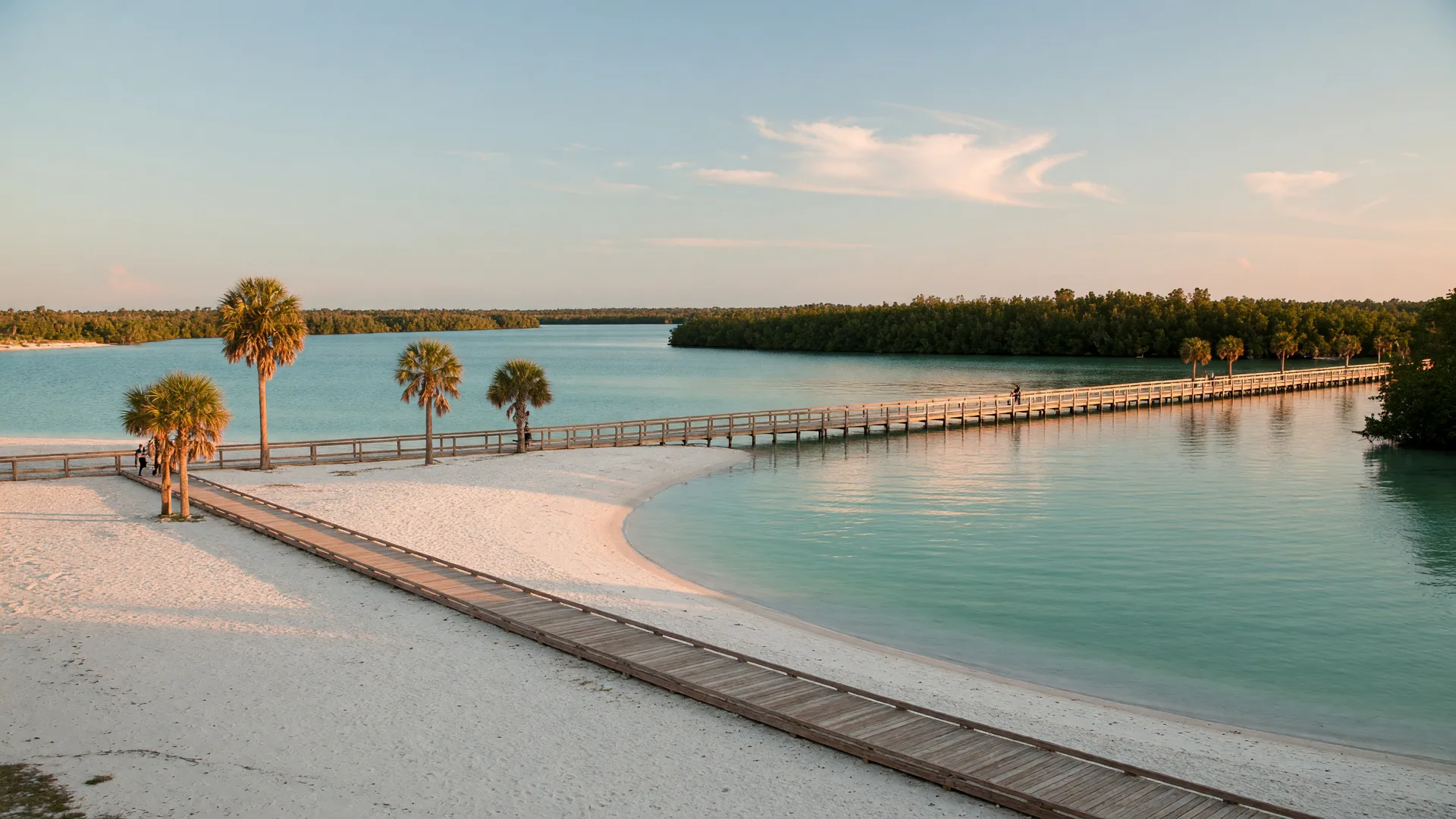 SunWest Park white-sand beach and lake in Hudson, Florida, at golden hour with a wooden boardwalk and palm trees