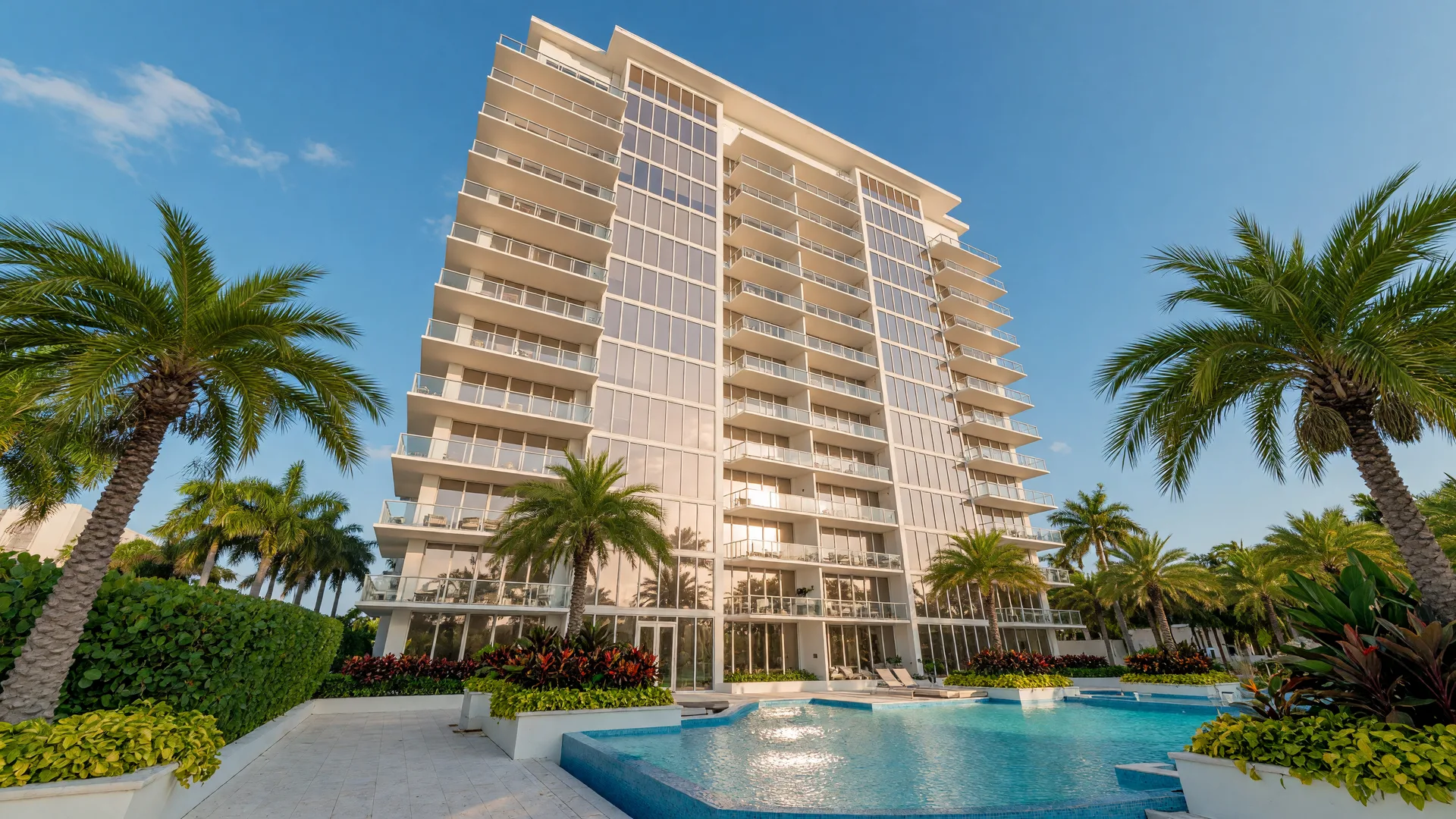 Modern luxury condominium tower in Naples, Florida with palm trees, pool, and clear blue sky