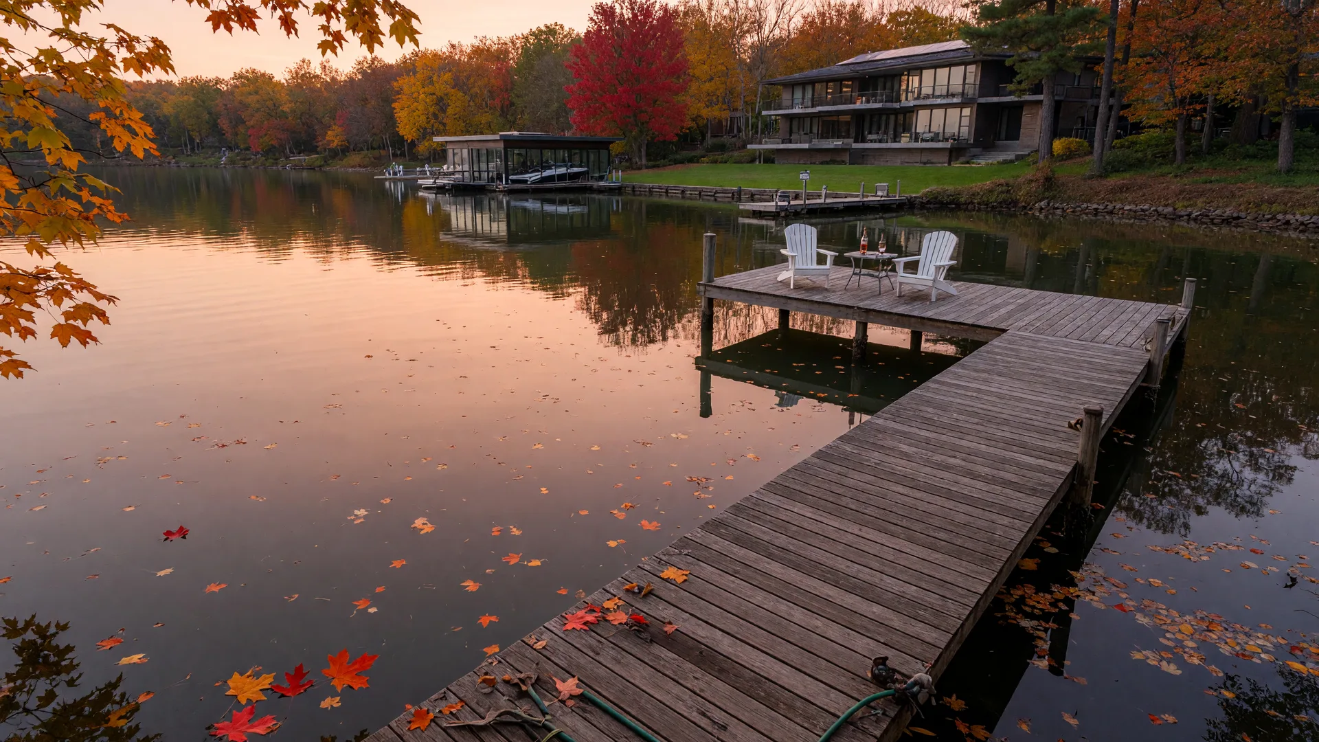 Wooden dock extending into calm Lake Norman water at golden hour with a modern lakefront home visible among autumn trees