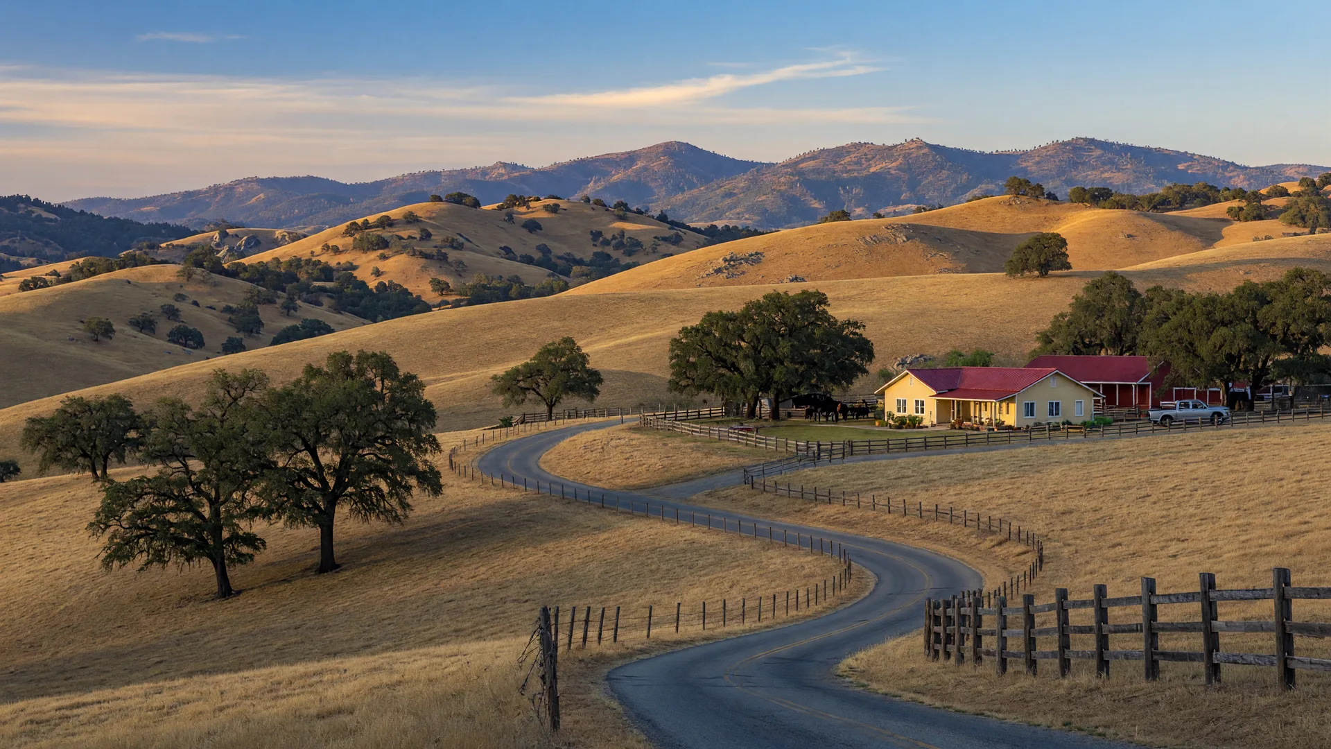Rolling oak-studded hills in Catheys Valley, California with a quiet country road winding between ranch properties and the Sierra Nevada foothills on the horizon at golden hour