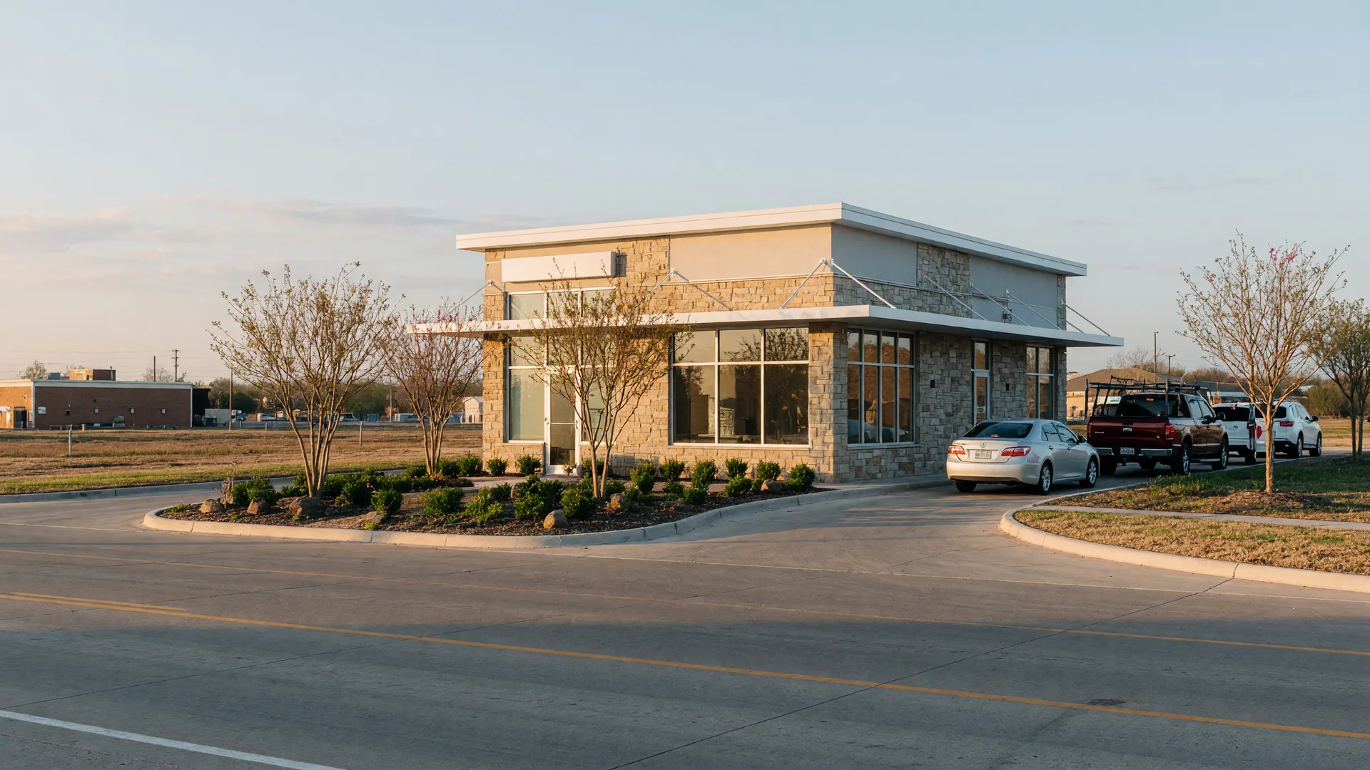 A modern coffee shop with a drive-thru lane on a broad commercial corridor in Paris, Texas in warm morning light