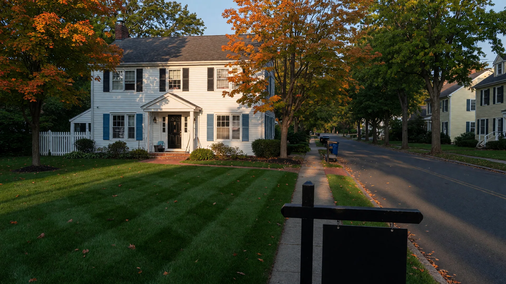 A tidy colonial home on a tree-lined New Jersey suburban street in late-September golden light, with maples showing the first fall color