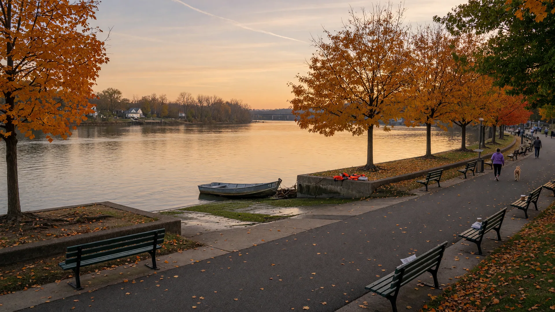 The Delaware River waterfront in Cinnaminson, New Jersey on a crisp October afternoon, with a paved promenade, wooden benches, and trees turning gold along the bank