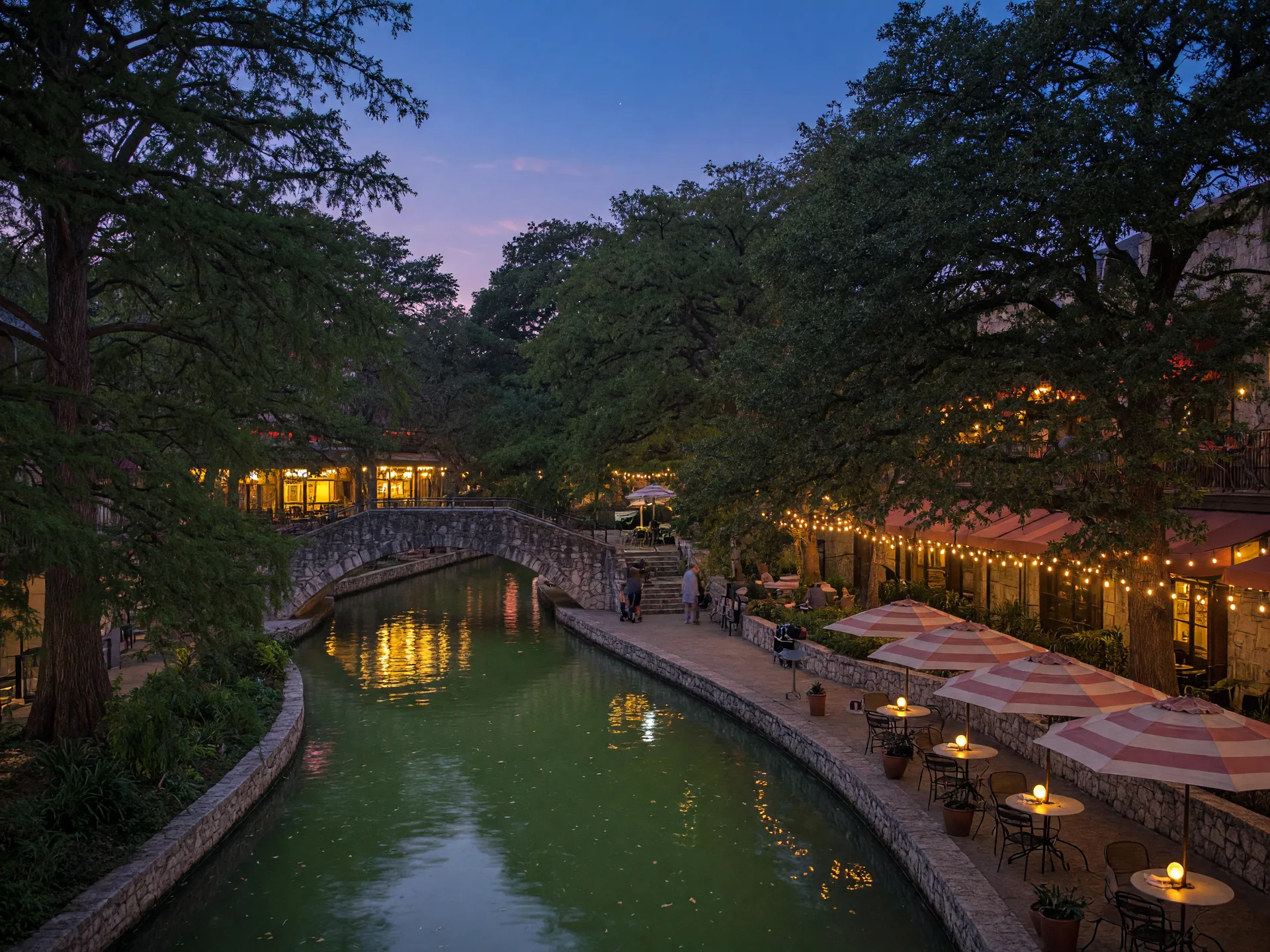 The San Antonio River Walk at dusk with cypress trees and glowing cafe lights