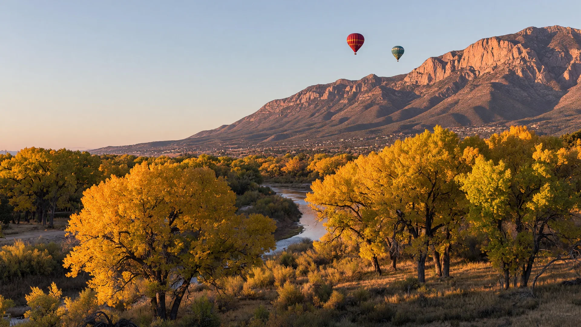 Golden cottonwoods along the Rio Grande with the Sandia Mountains at sunset and a few hot air balloons in a clear October sky