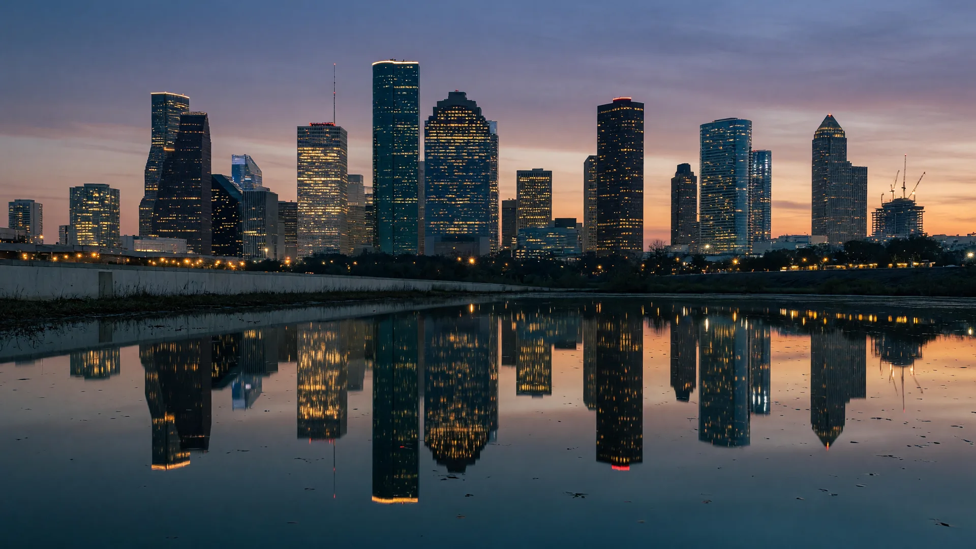 The downtown Houston skyline at dusk, reflected in a calm waterway