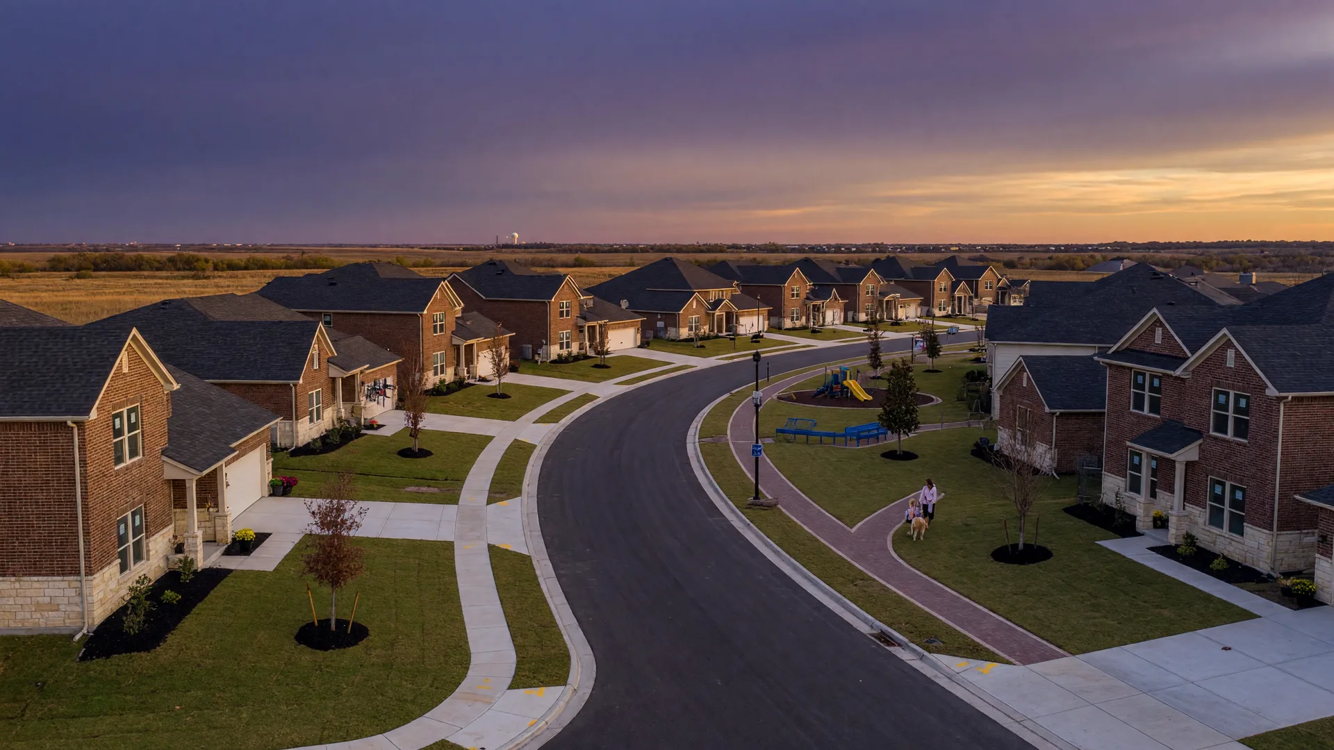 Representative image of a new North Texas home community at dusk, with curving streets, young trees, and a walking trail